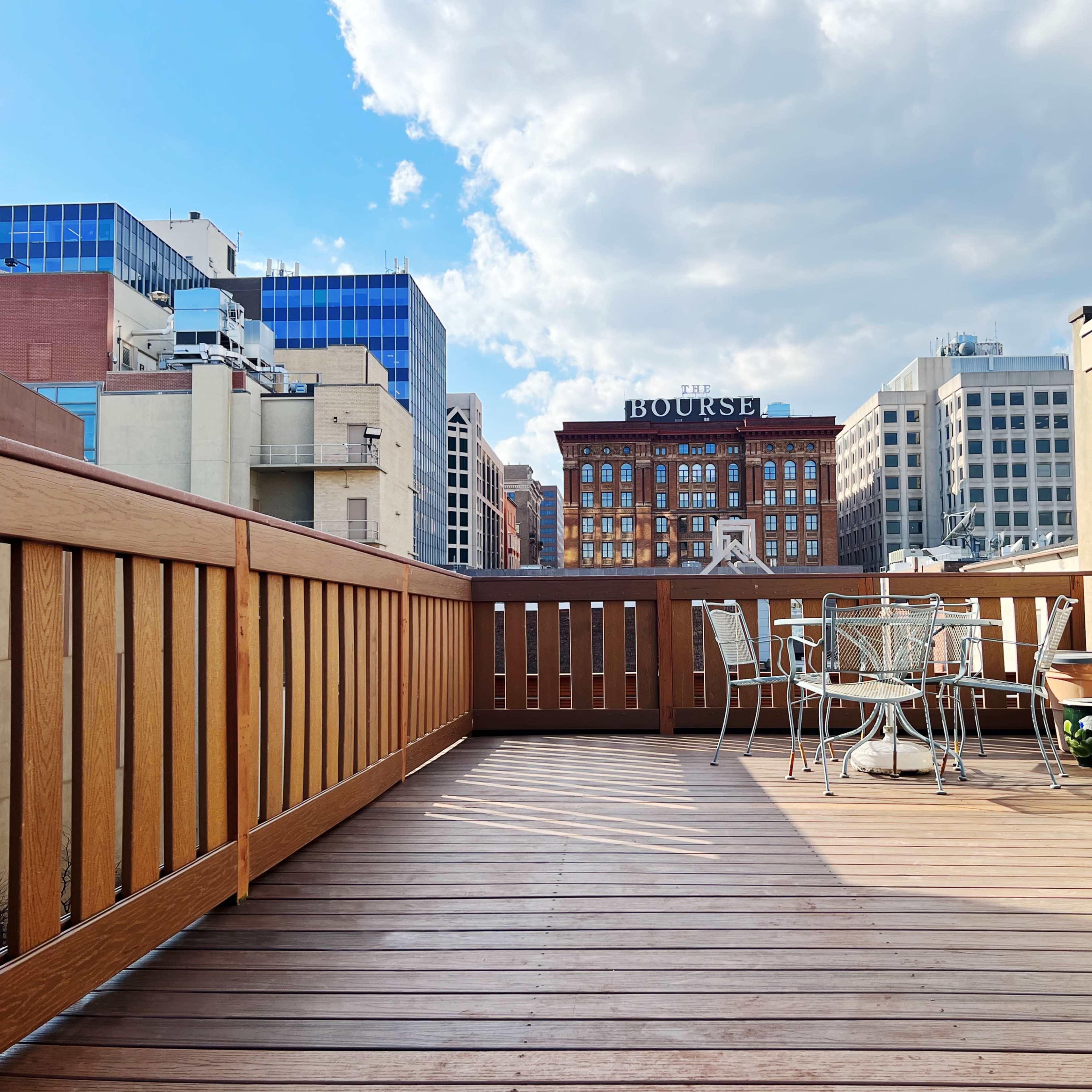 A wooden deck with a table and chairs, overlooking buildings and a clear sky.