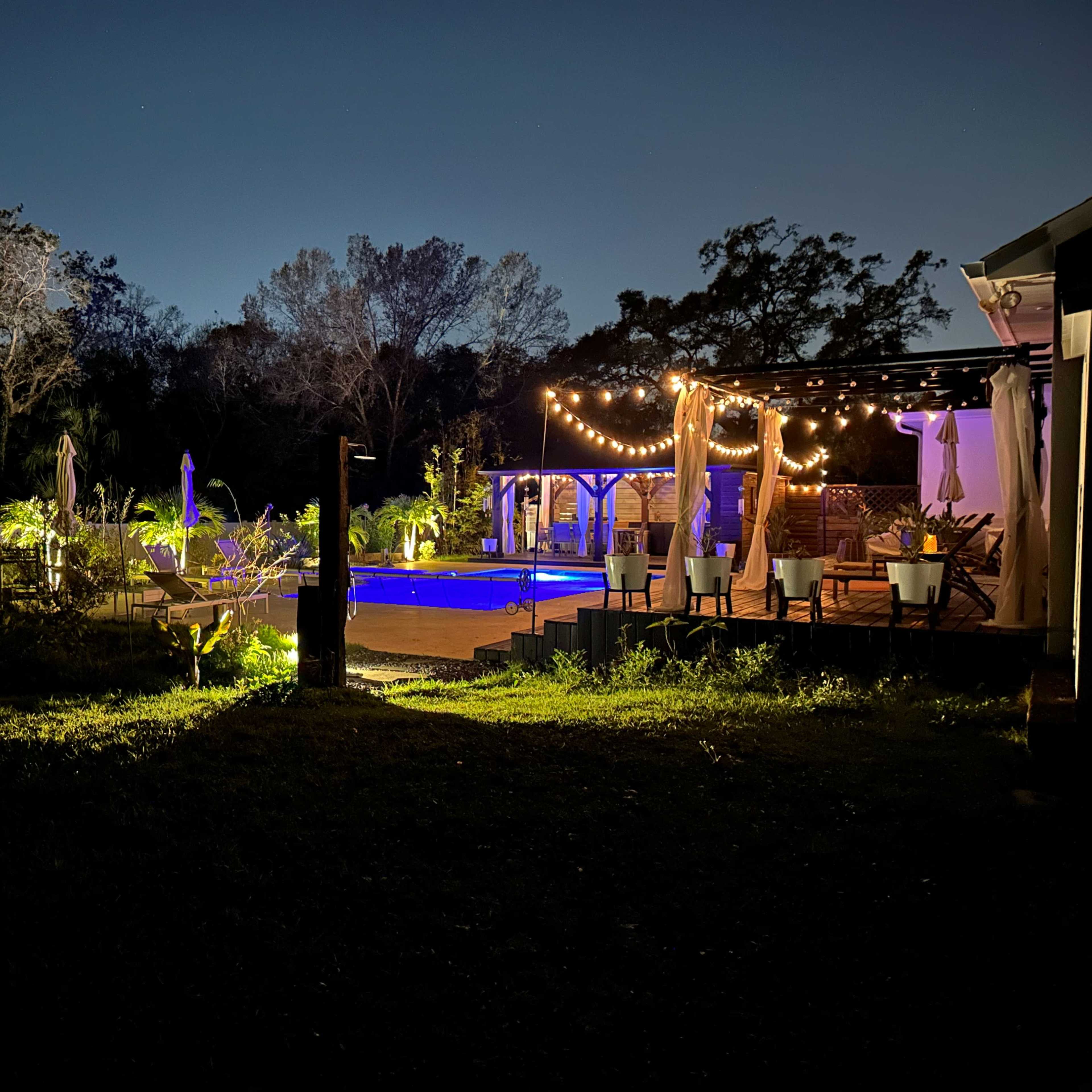 A dimly lit backyard with a pool surrounded by string lights and plants.