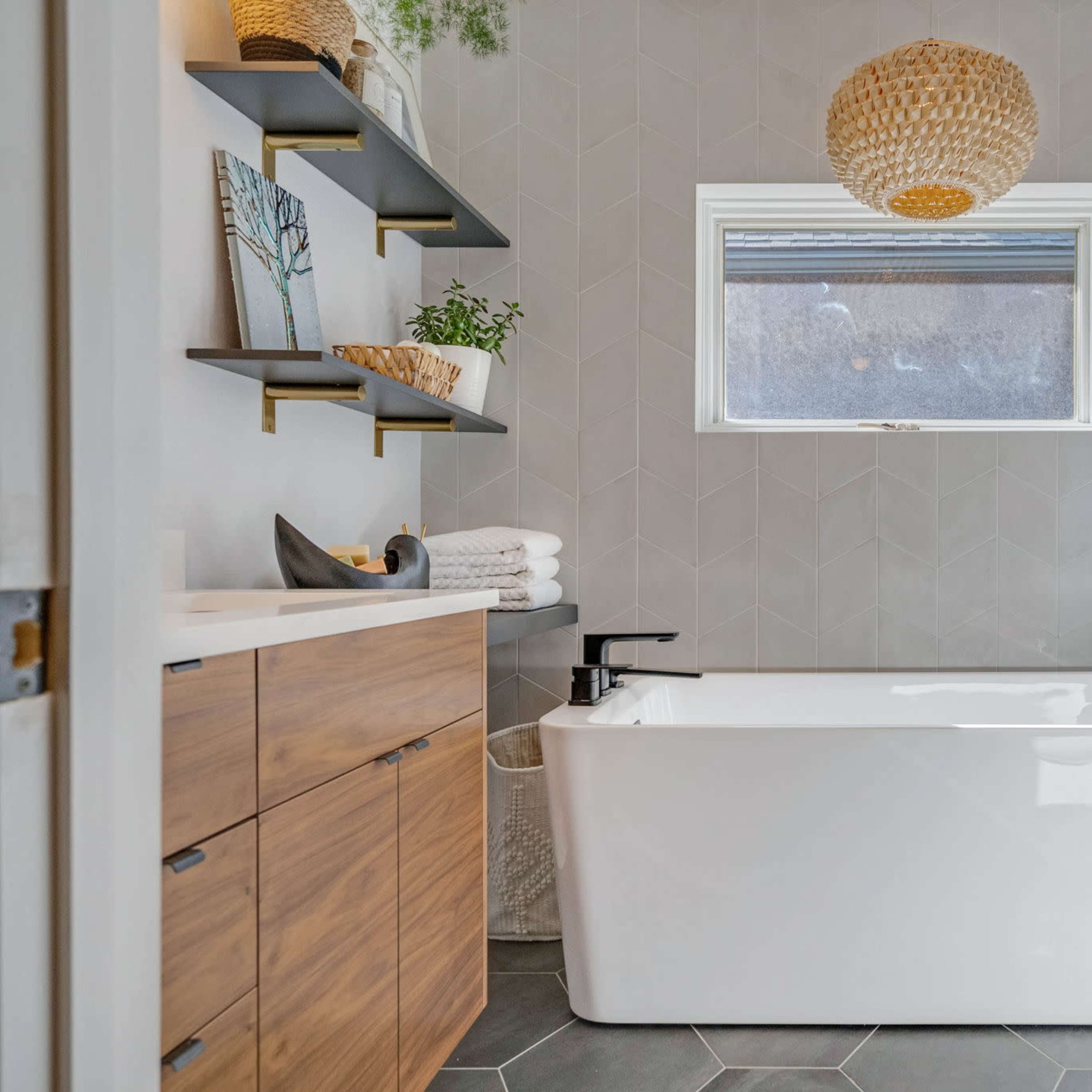 A modern bathroom features a freestanding bathtub, wooden cabinetry, and geometric tile flooring, illuminated by natural light from a window.