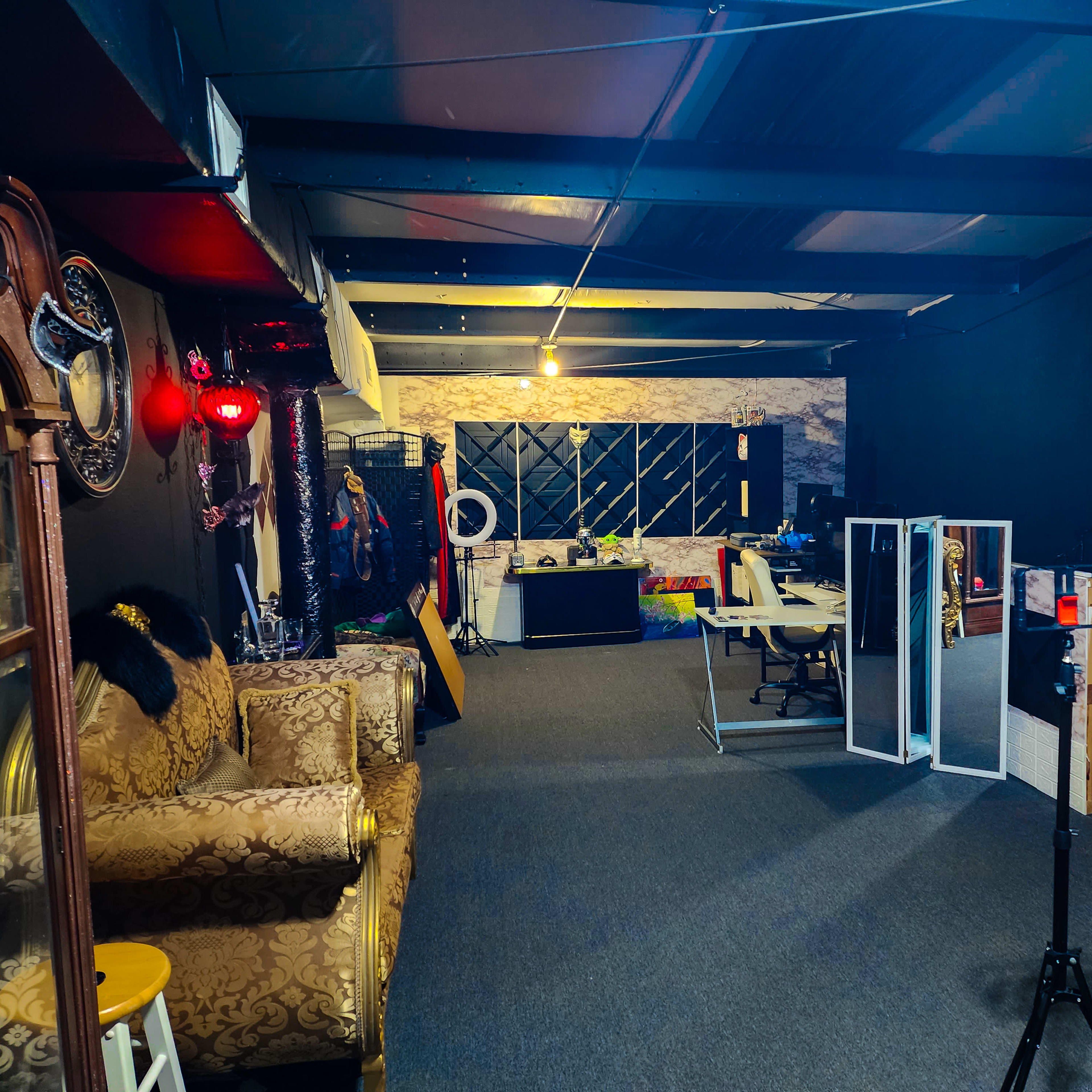 A spacious interior room with a sofa, a desk area, and partitions dividing different sections, all set against dark walls and a carpeted floor.