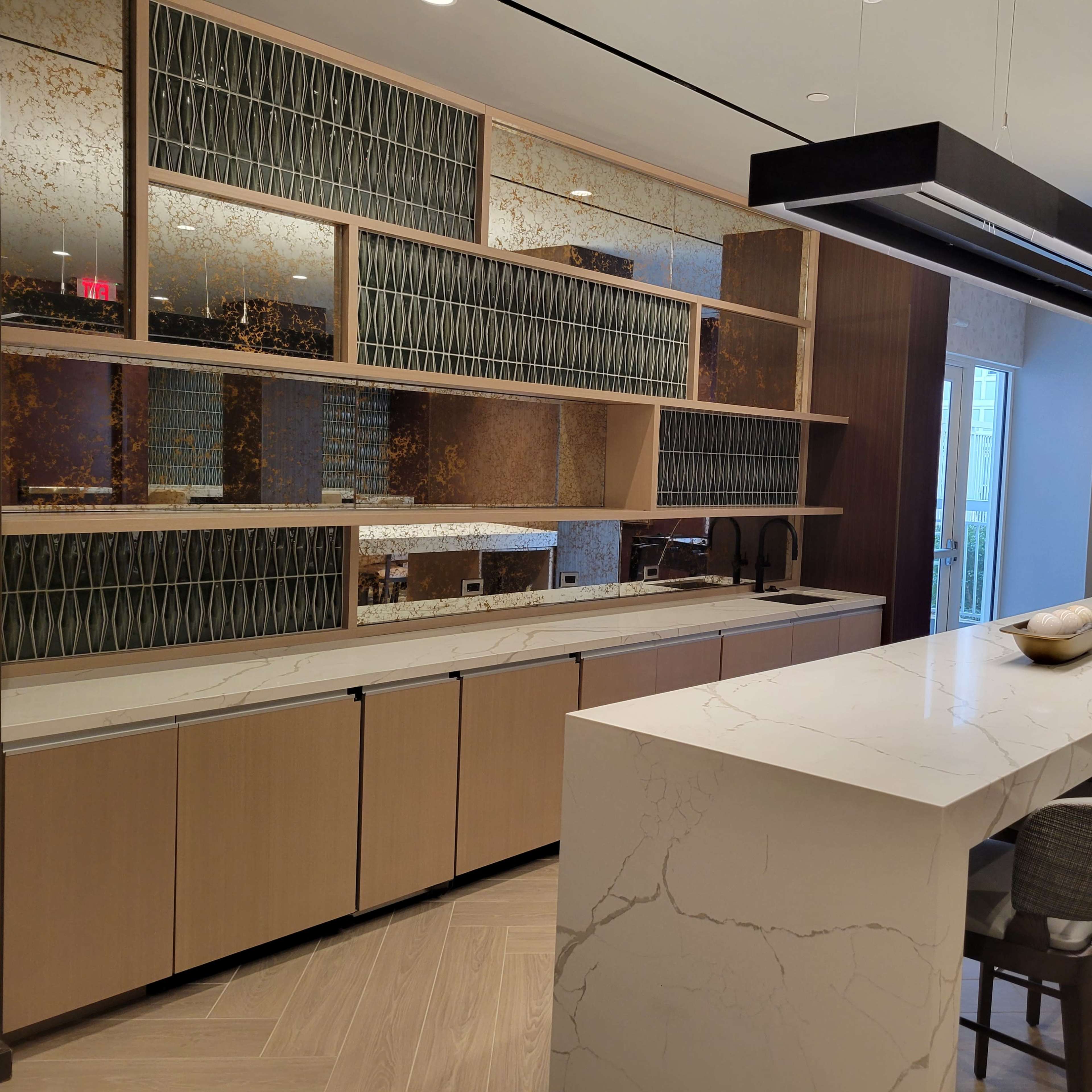 A modern kitchen features a long marble island with bar seating and decorative shelves above a sleek countertop.
