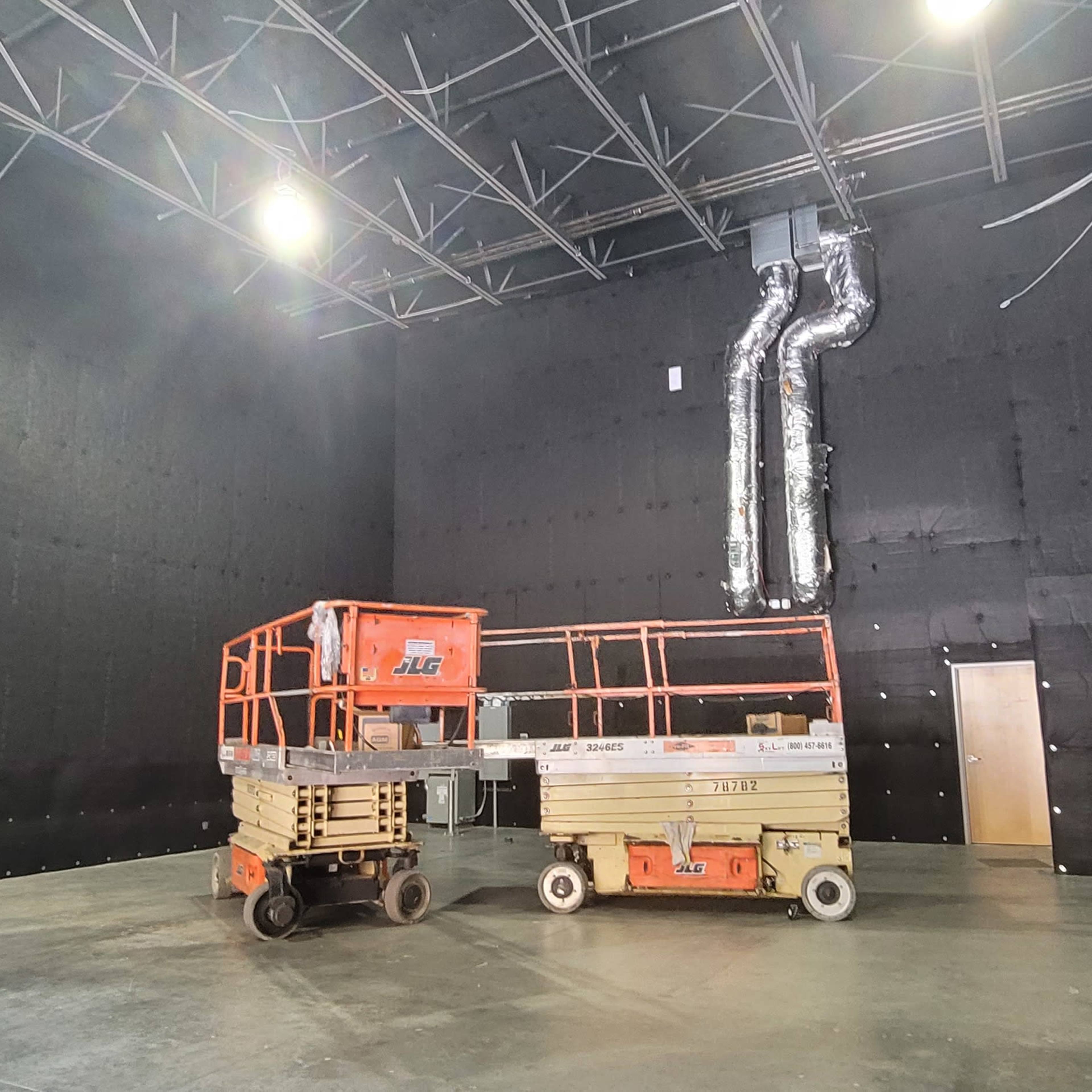 A large, empty room with black walls and two scissor lift platforms positioned on the concrete floor.