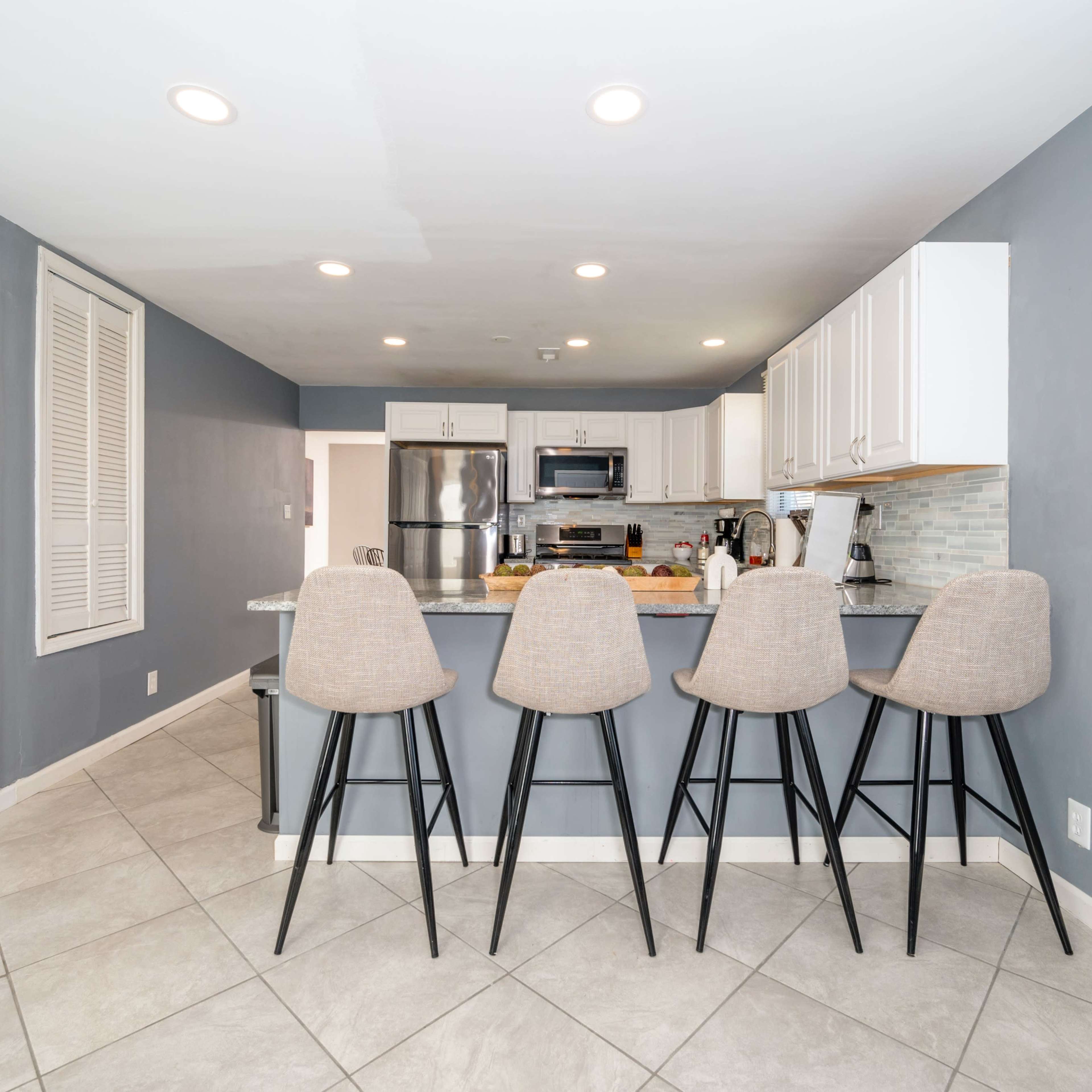 A modern kitchen features a gray color scheme with white cabinets and four high stools positioned at a breakfast bar.