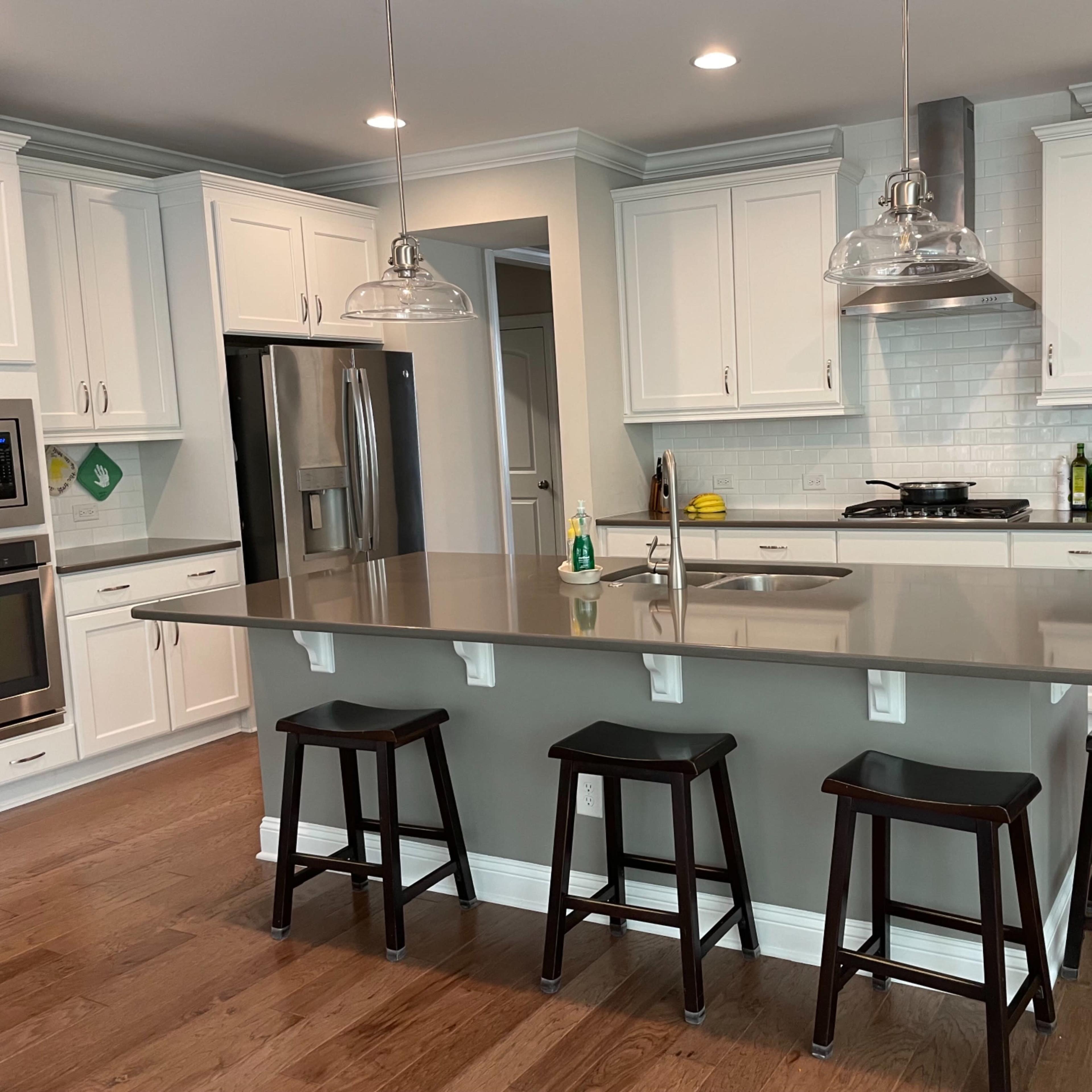 The kitchen features white cabinetry, a large island with bar stools, and stainless steel appliances.