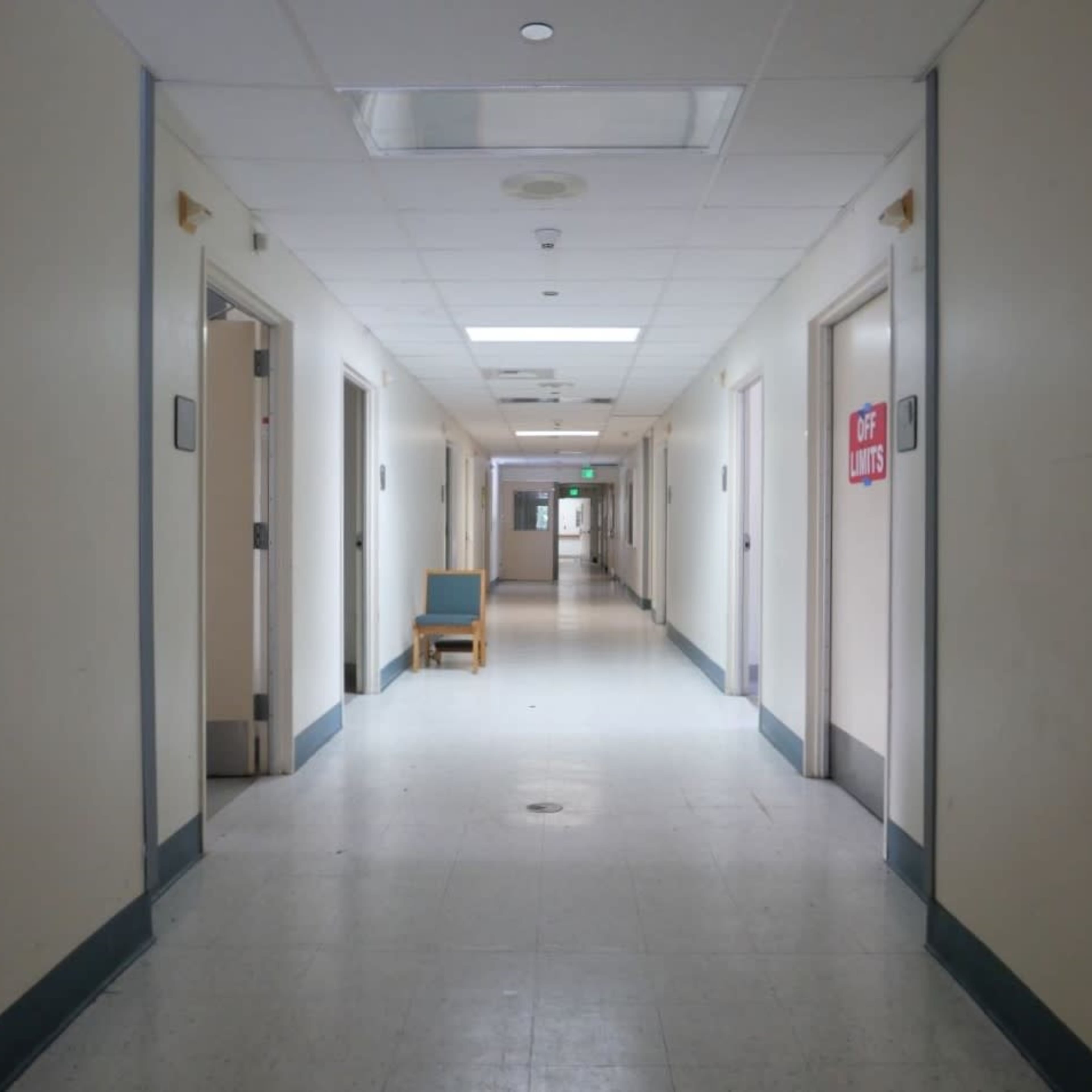 A long, empty hallway with closed doors on either side and a chair positioned against one wall.