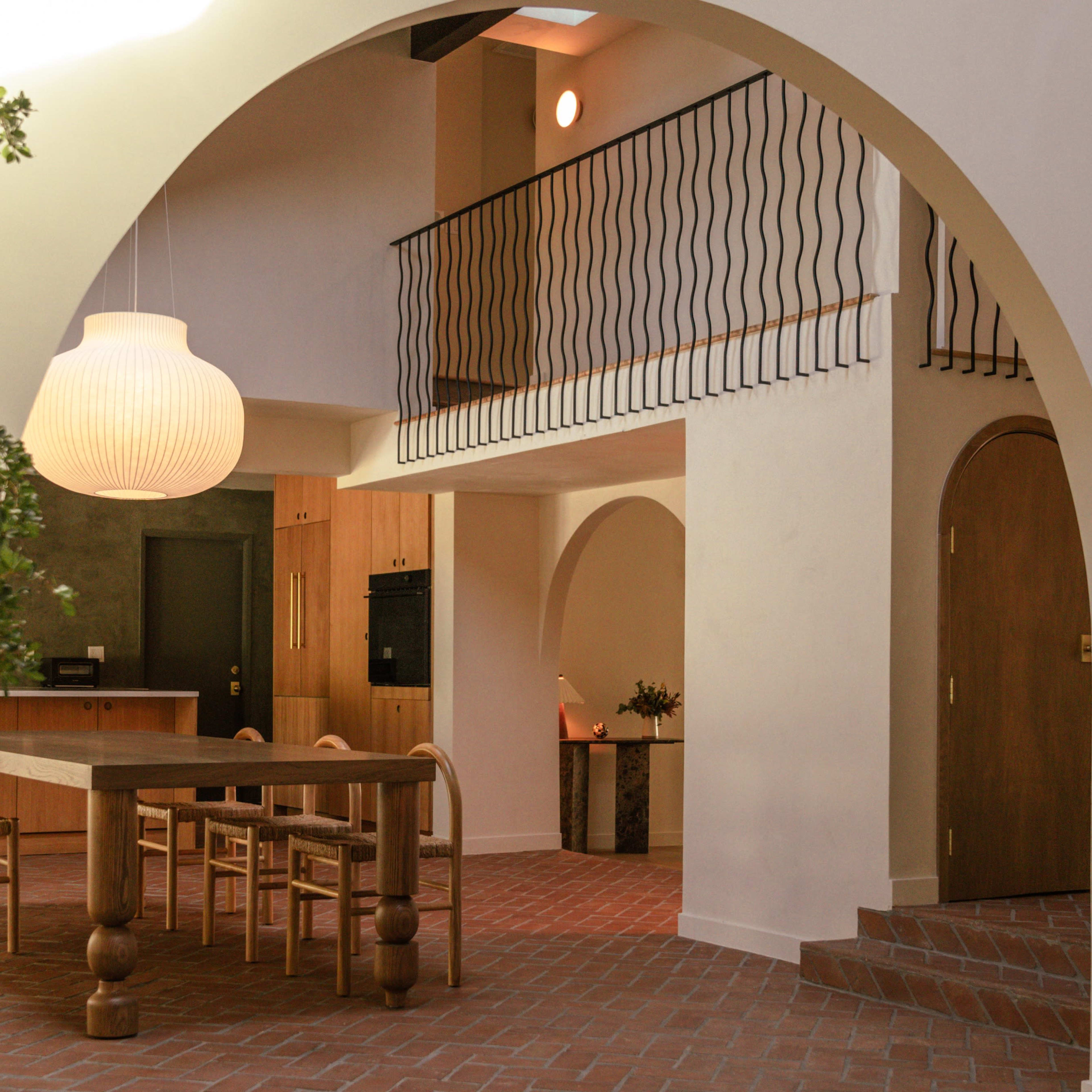 A modern interior space featuring arched openings, a wooden dining table, a spiral staircase, and a large pendant light.