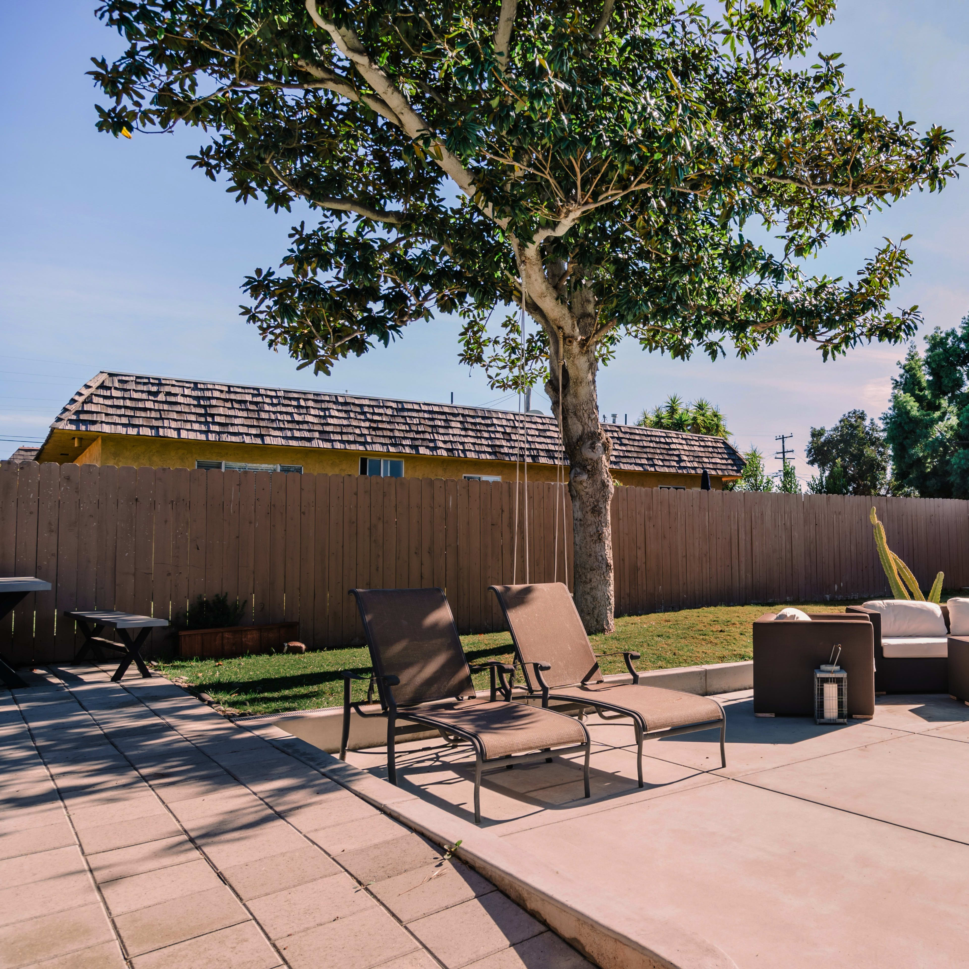 A backyard patio area with lounge chairs and a seating arrangement near a green lawn and a small shed in the background.