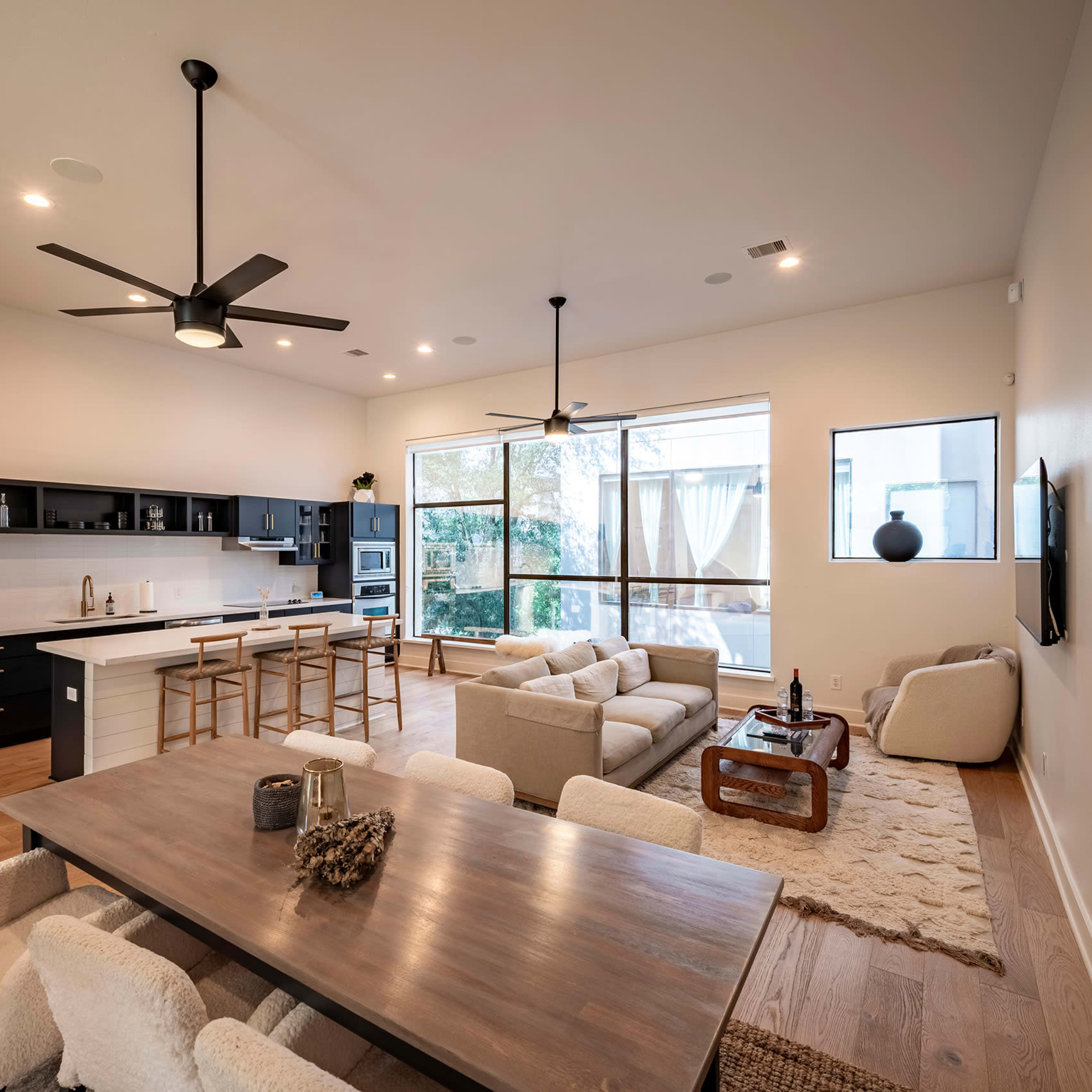 A modern open-concept living space with a kitchen, dining area, and seating arrangement by large windows.
