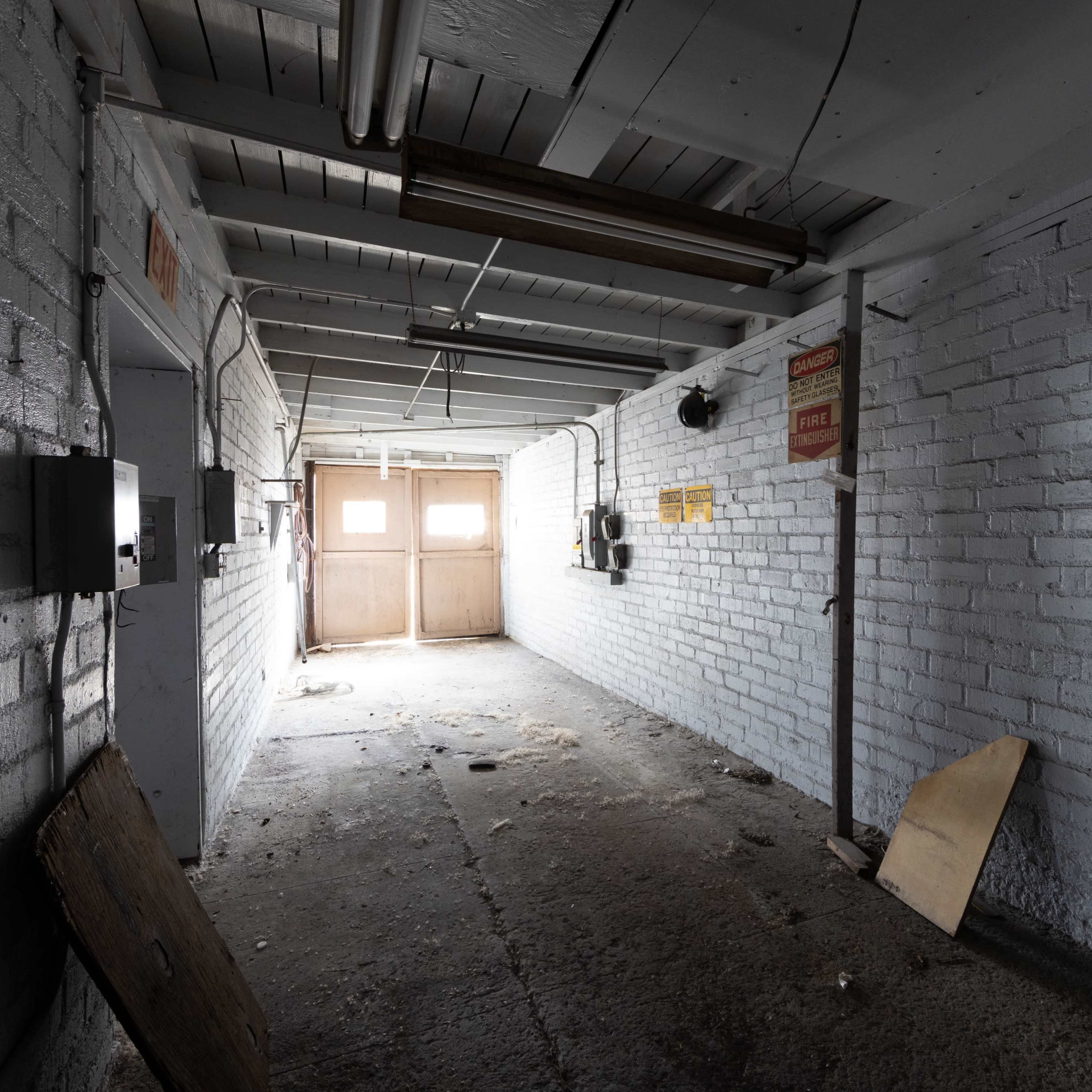 A dimly lit, abandoned corridor with concrete floors and white brick walls.