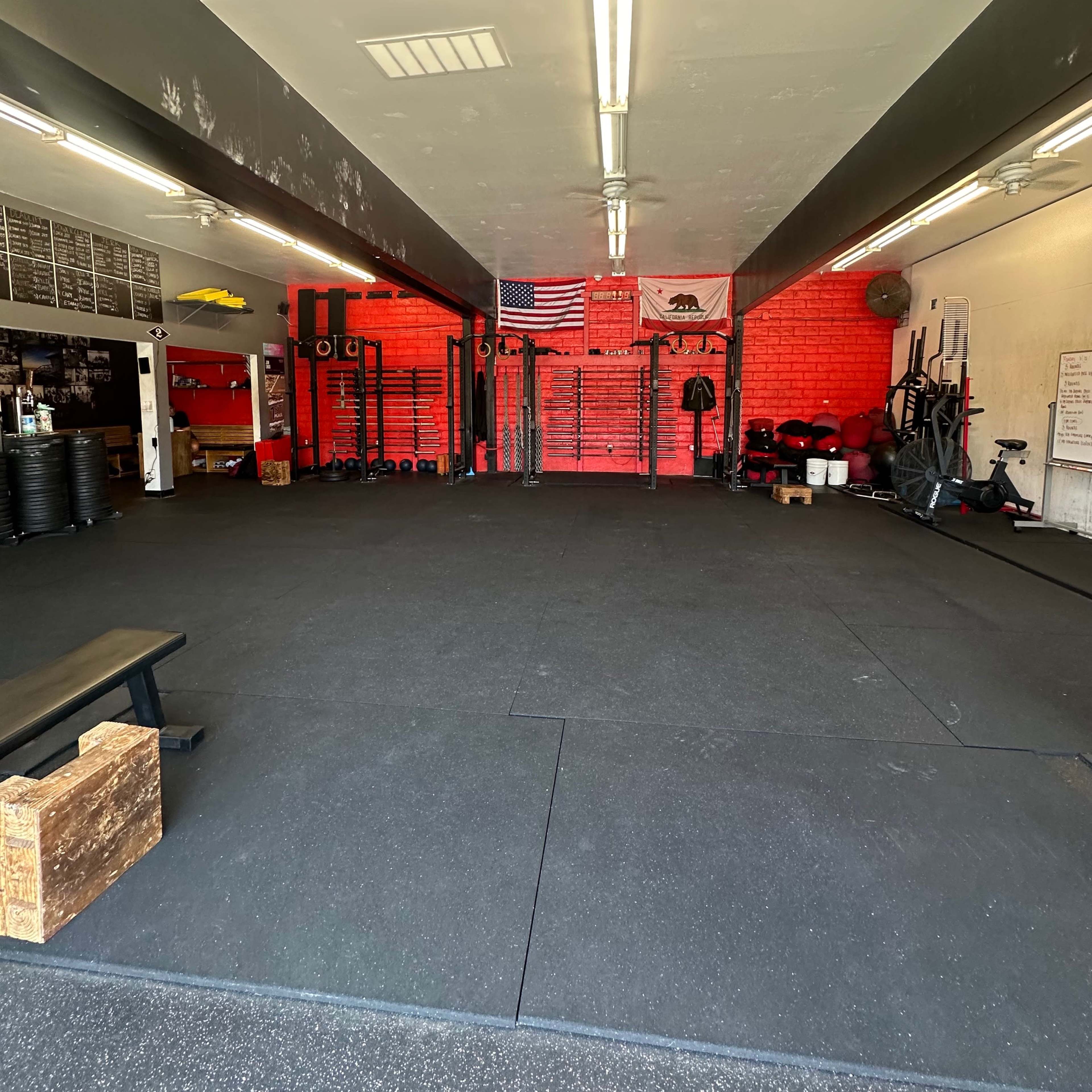 A fitness gym with rubber flooring, wall-mounted equipment, and an American flag displayed against a red wall.