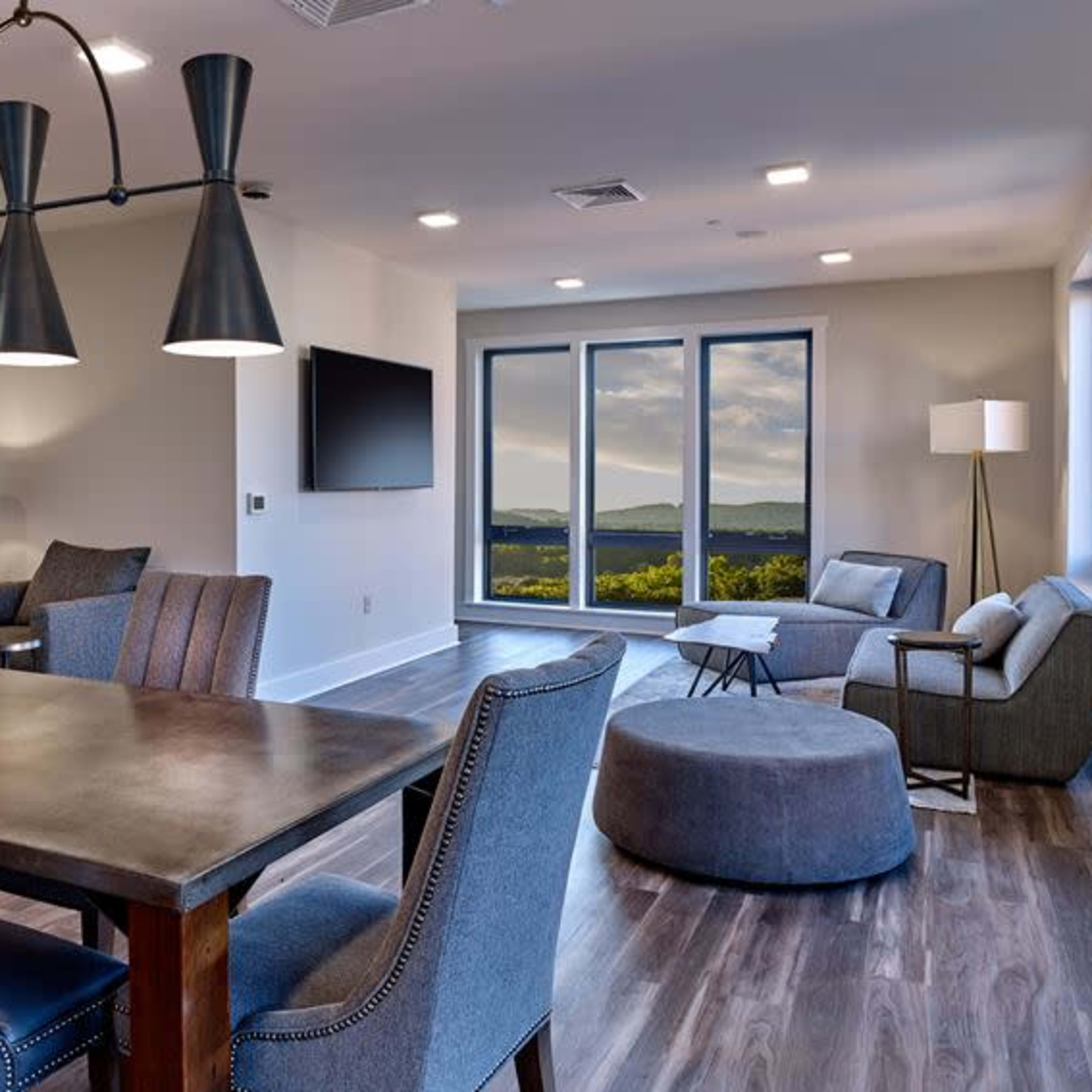 A modern living space features a dining table, lounge seating, and large windows showcasing a mountainous view.