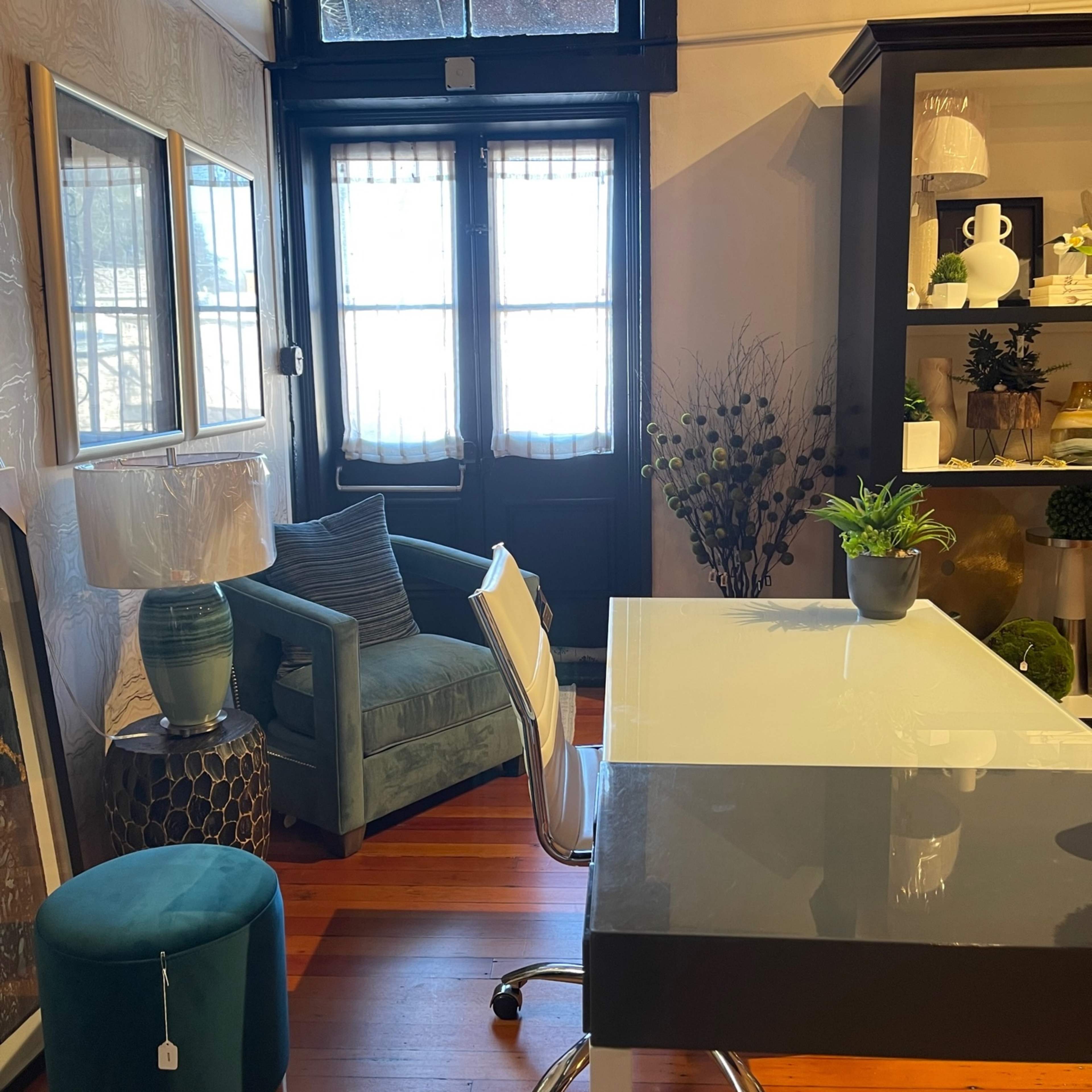 A modern office space featuring a glass desk, a blue chair, and large windows with wooden flooring.