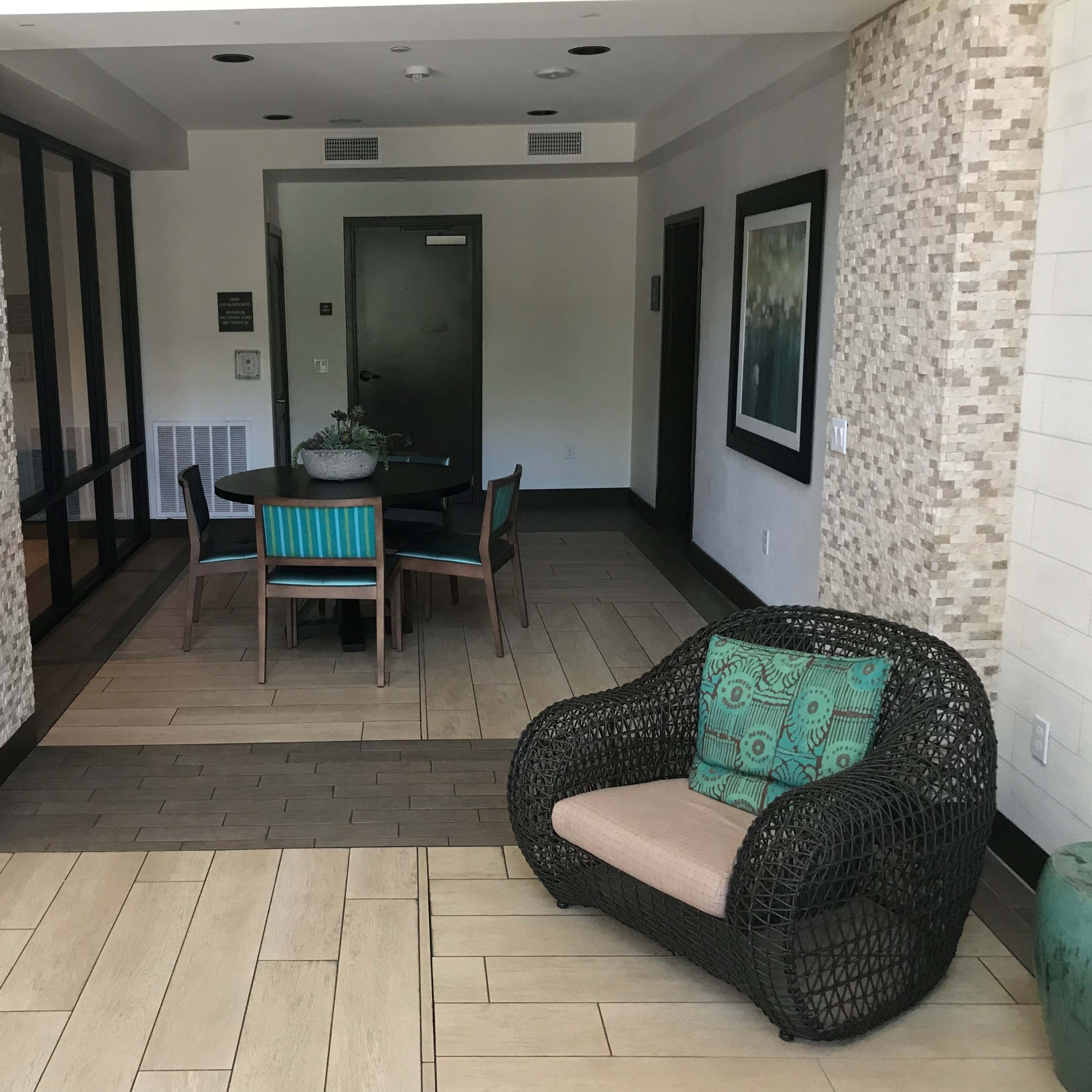 A modern lobby area featuring a round dining table with upholstered chairs and a large wicker chair with cushions.