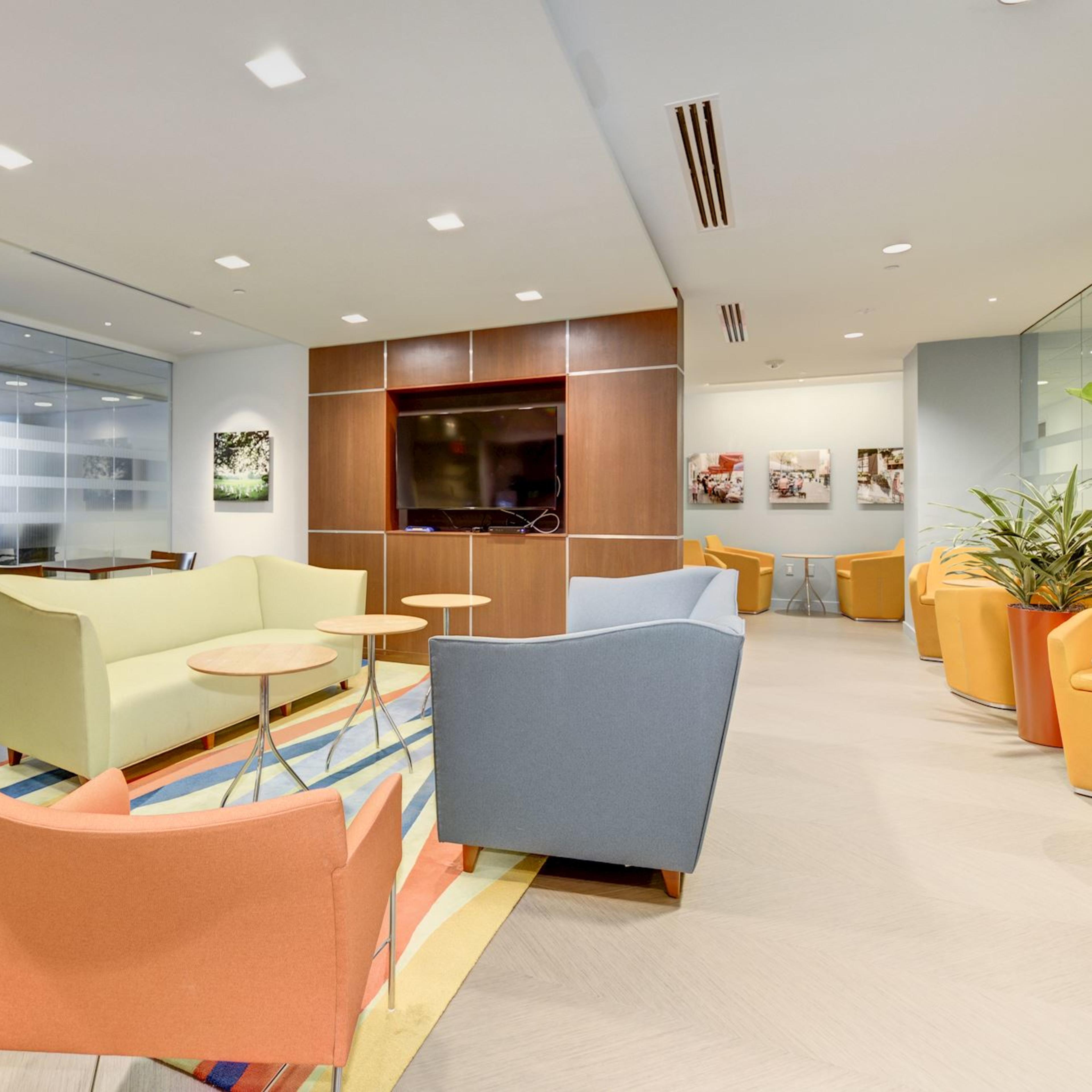A modern lounge area with colorful seating, a television mounted on a wooden wall, and large potted plants.
