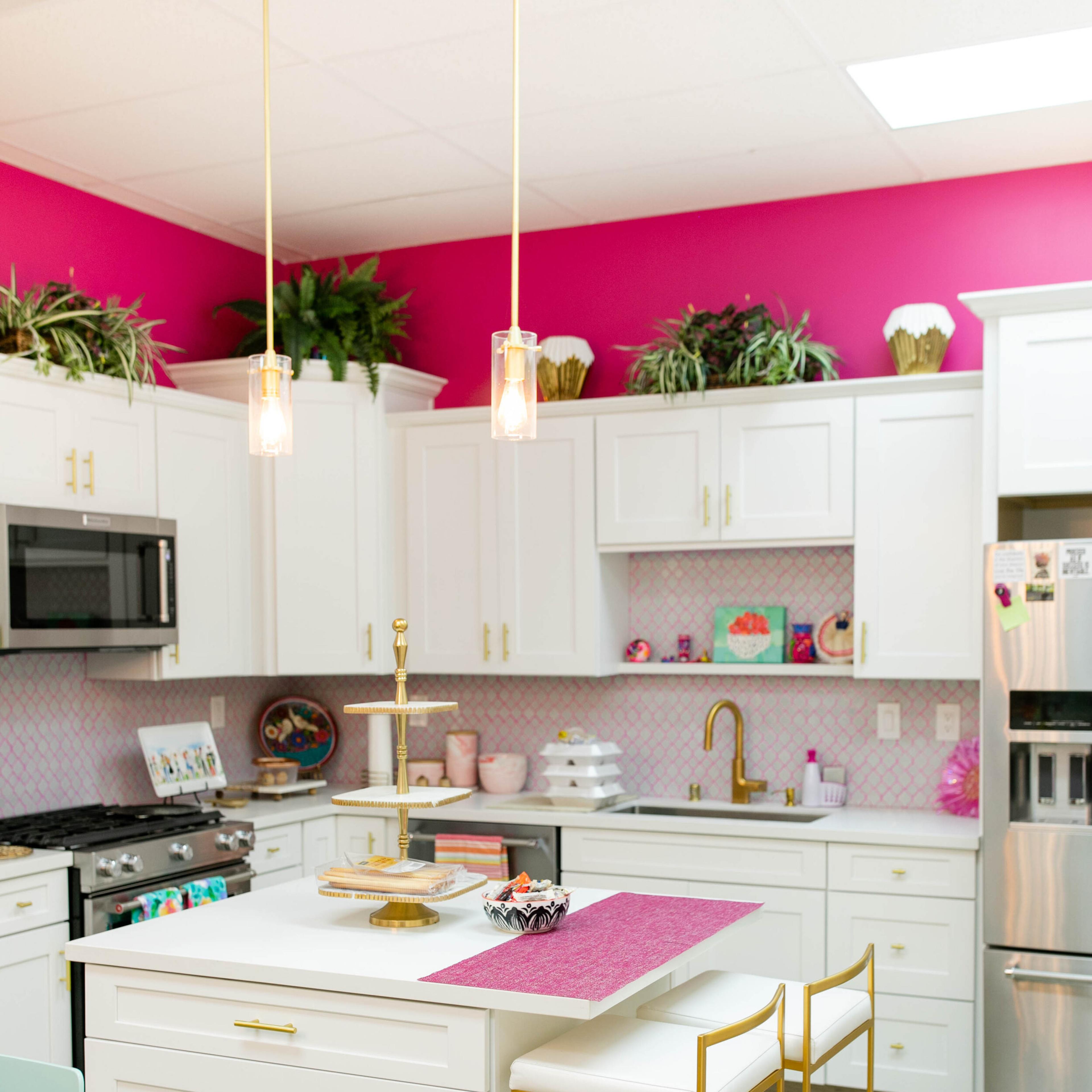 The kitchen features white cabinetry, gold accents, and bright pink walls, along with a central island and modern appliances.