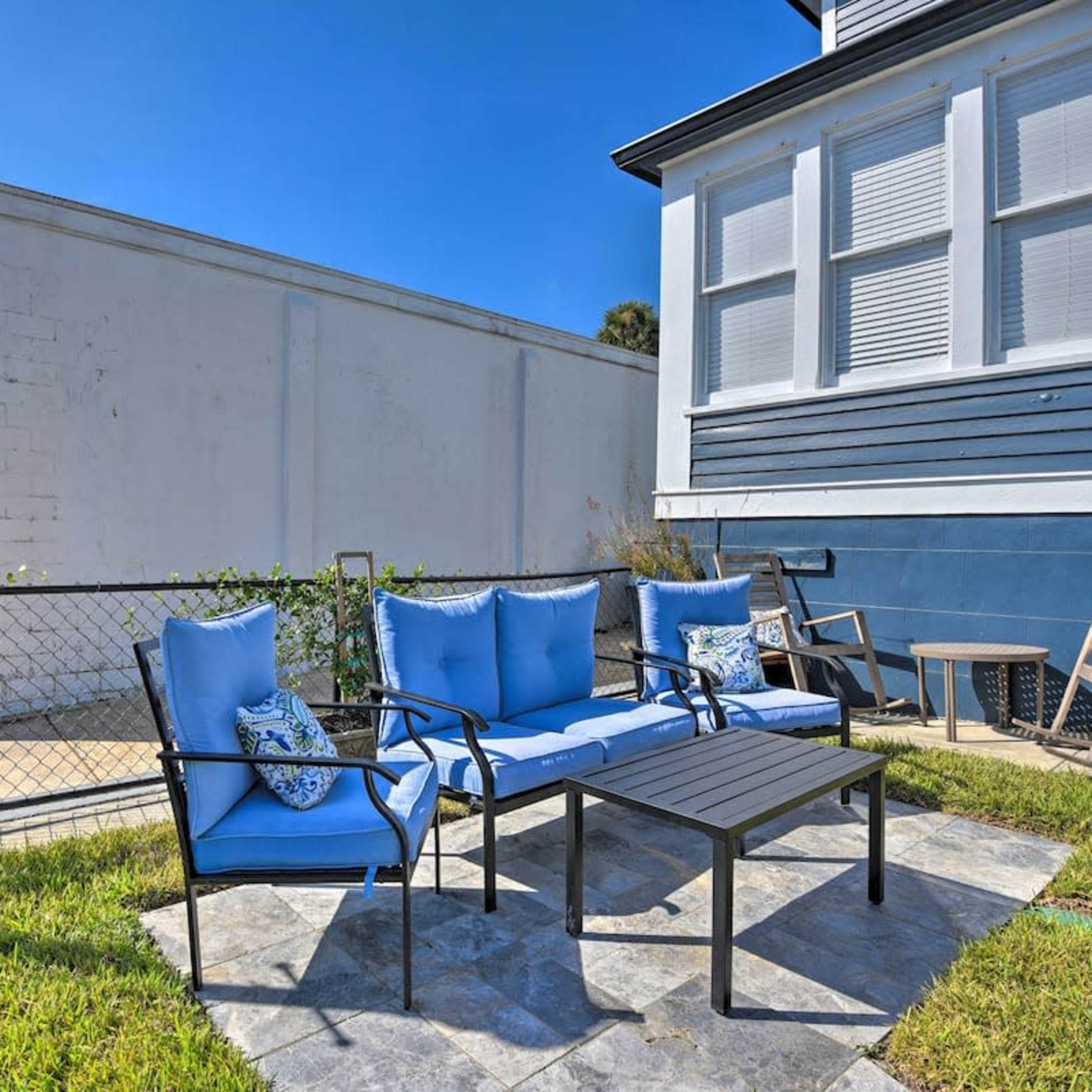 A patio area features blue chairs and a black table surrounded by green grass and a decorative fence.