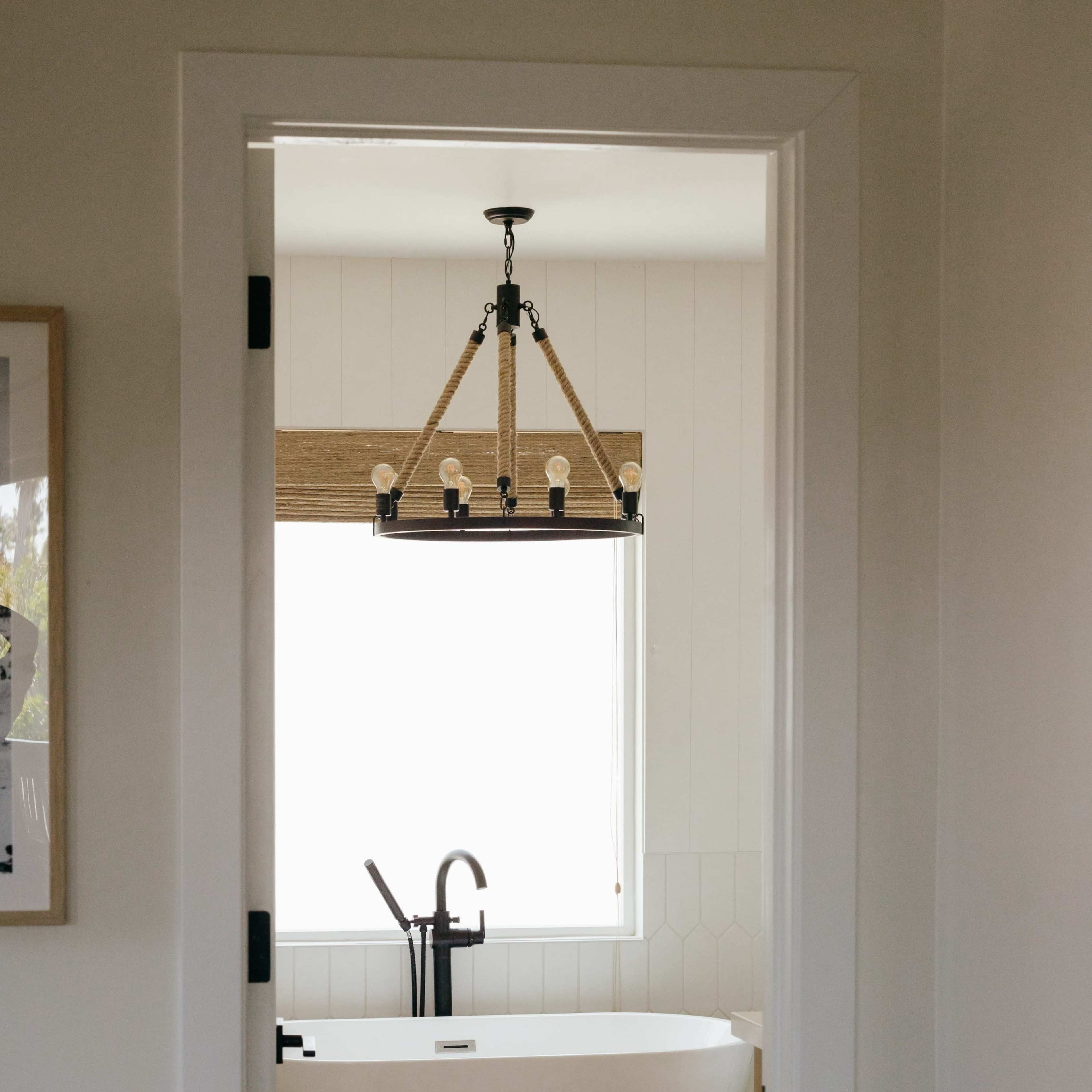 A modern bathroom features a freestanding tub, a window with natural light, and a stylish chandelier above.