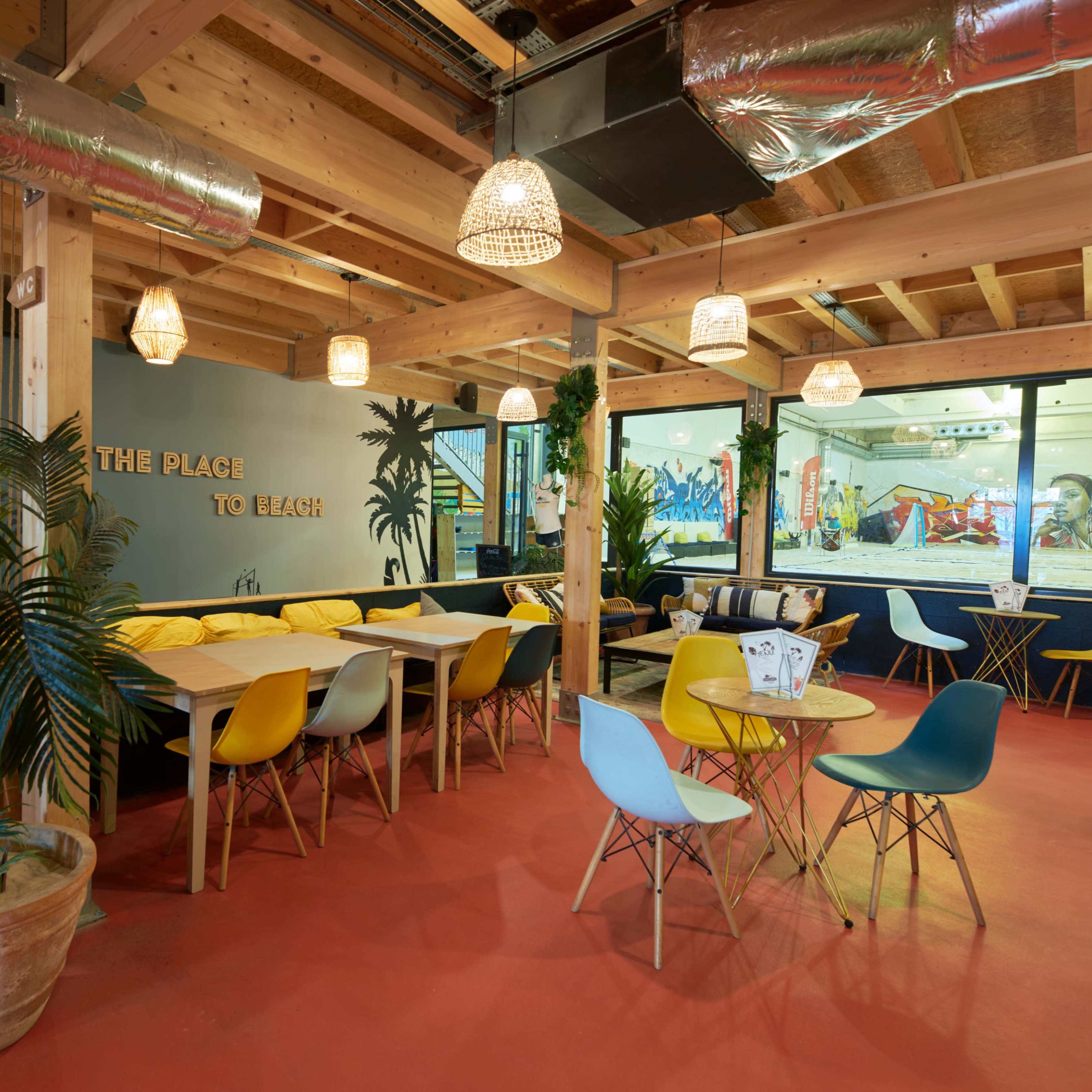 A modern indoor dining area with wooden beams, colorful chairs, and large windows featuring a view of a play area.
