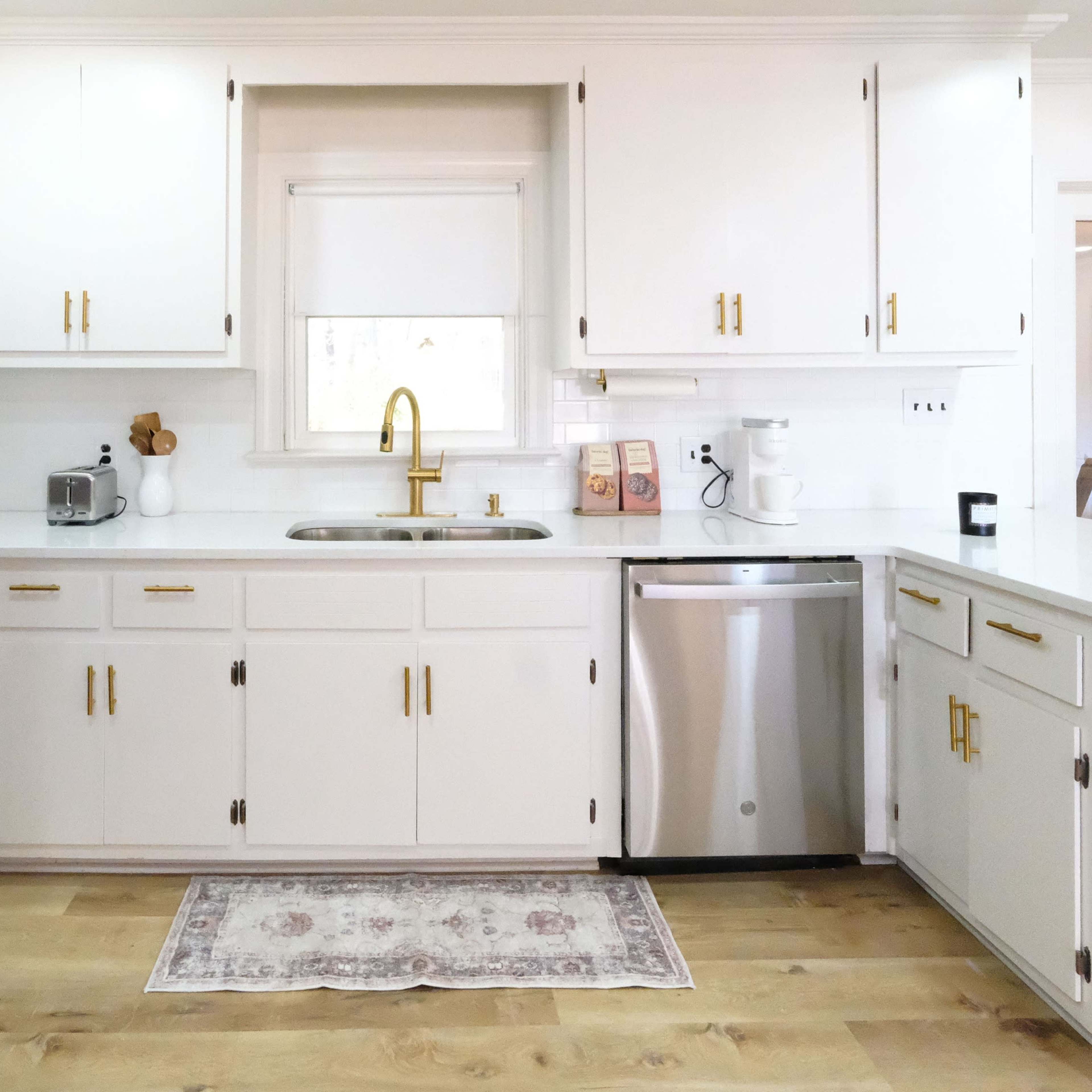 A modern kitchen with white cabinets, stainless steel appliances, and a central sink under a window.