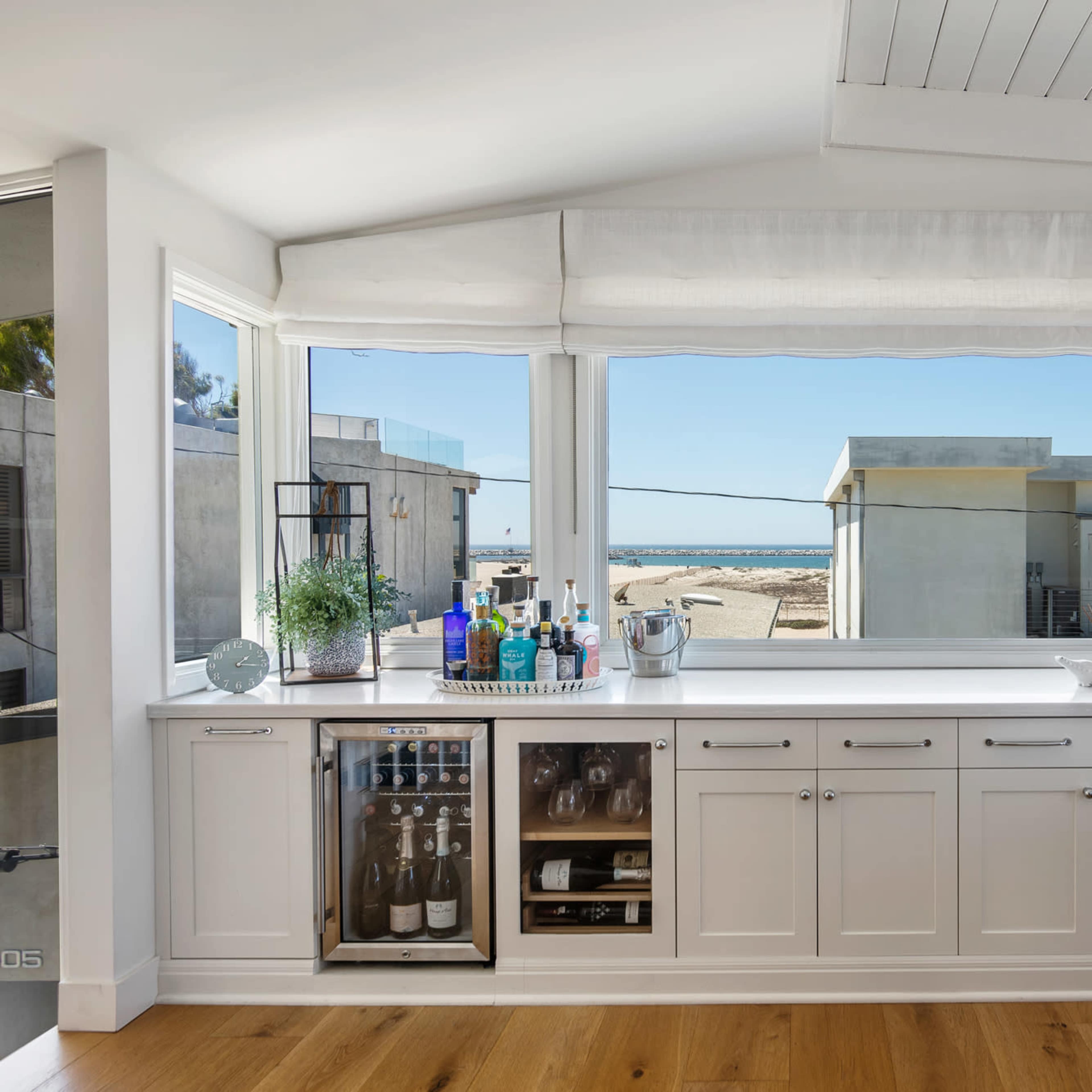 A well-lit interior showcases a sleek bar area with an array of beverages and a view of the ocean through large windows.