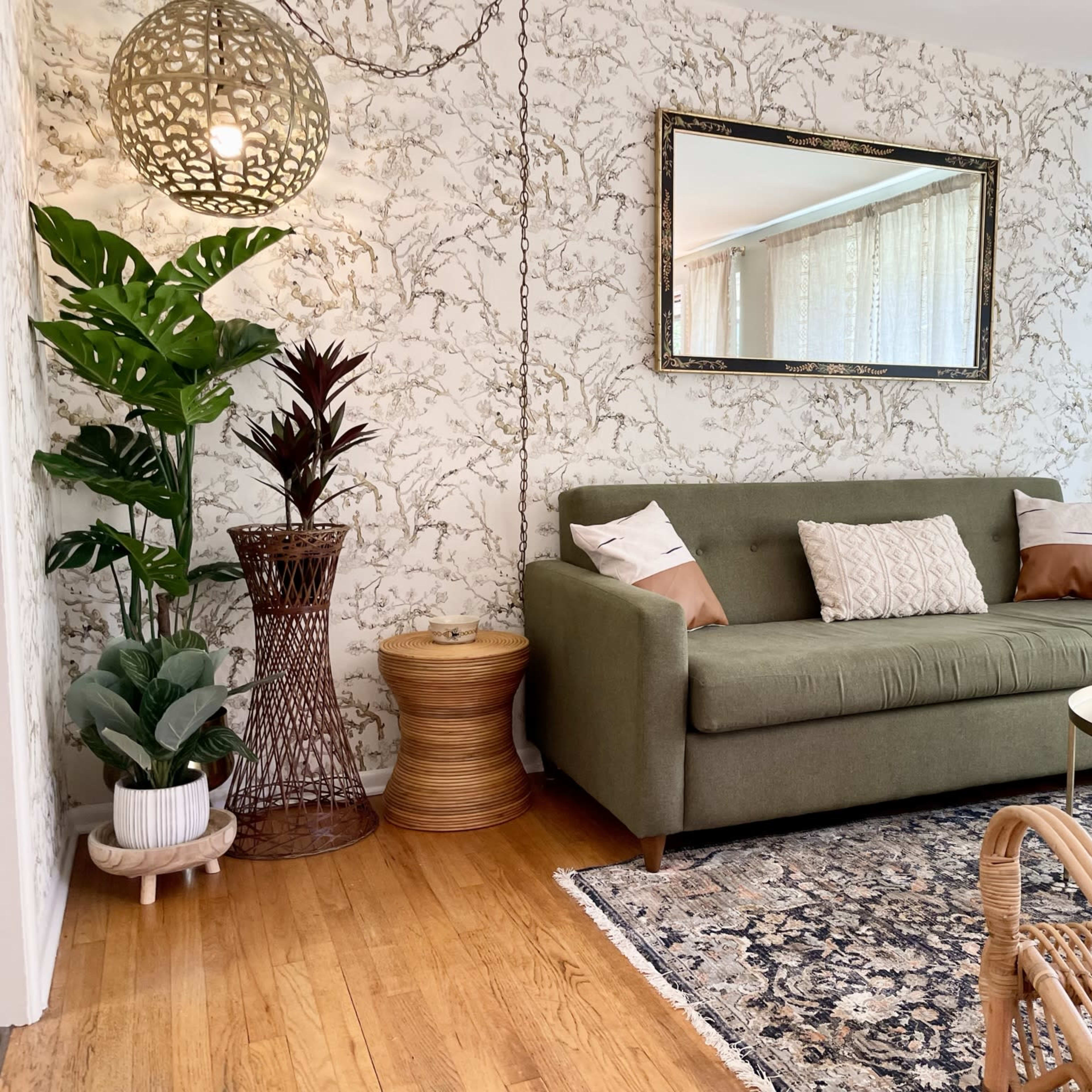A cozy living room with a green sofa, a round coffee table, and decorative plants against a patterned wallpaper backdrop.