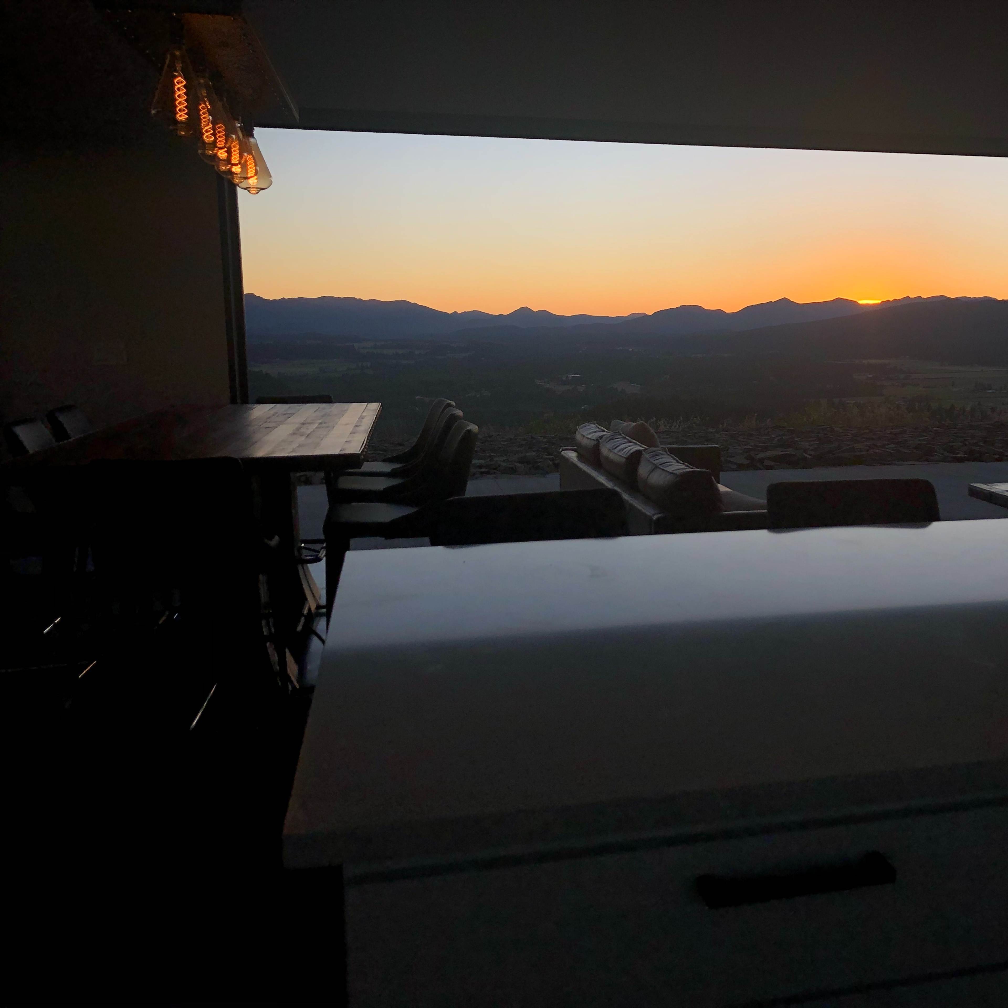A sunset is visible over mountains through an open window, with a dining area in the foreground.