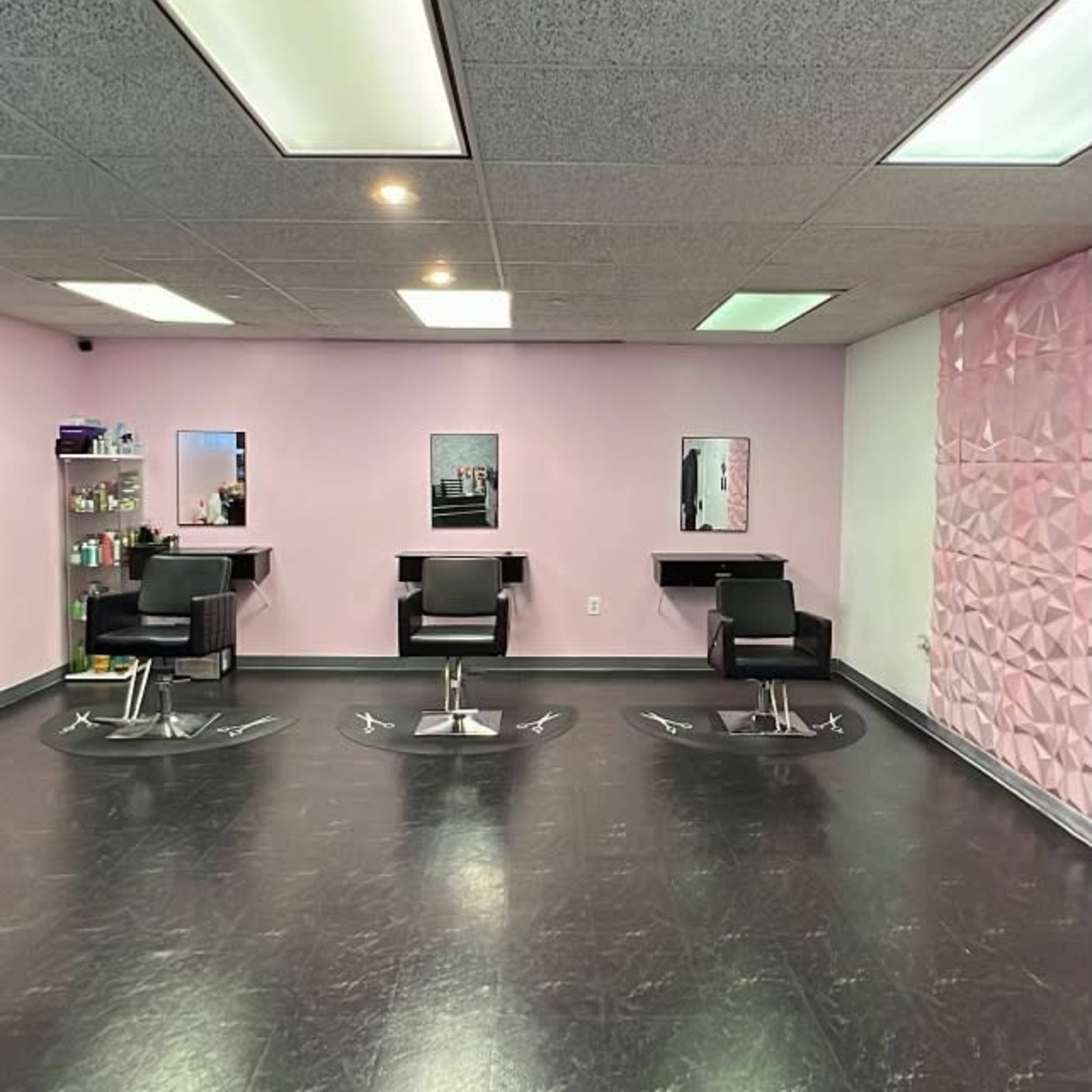 A hair salon interior with three styling chairs, mirrors, and a textured pink wall.