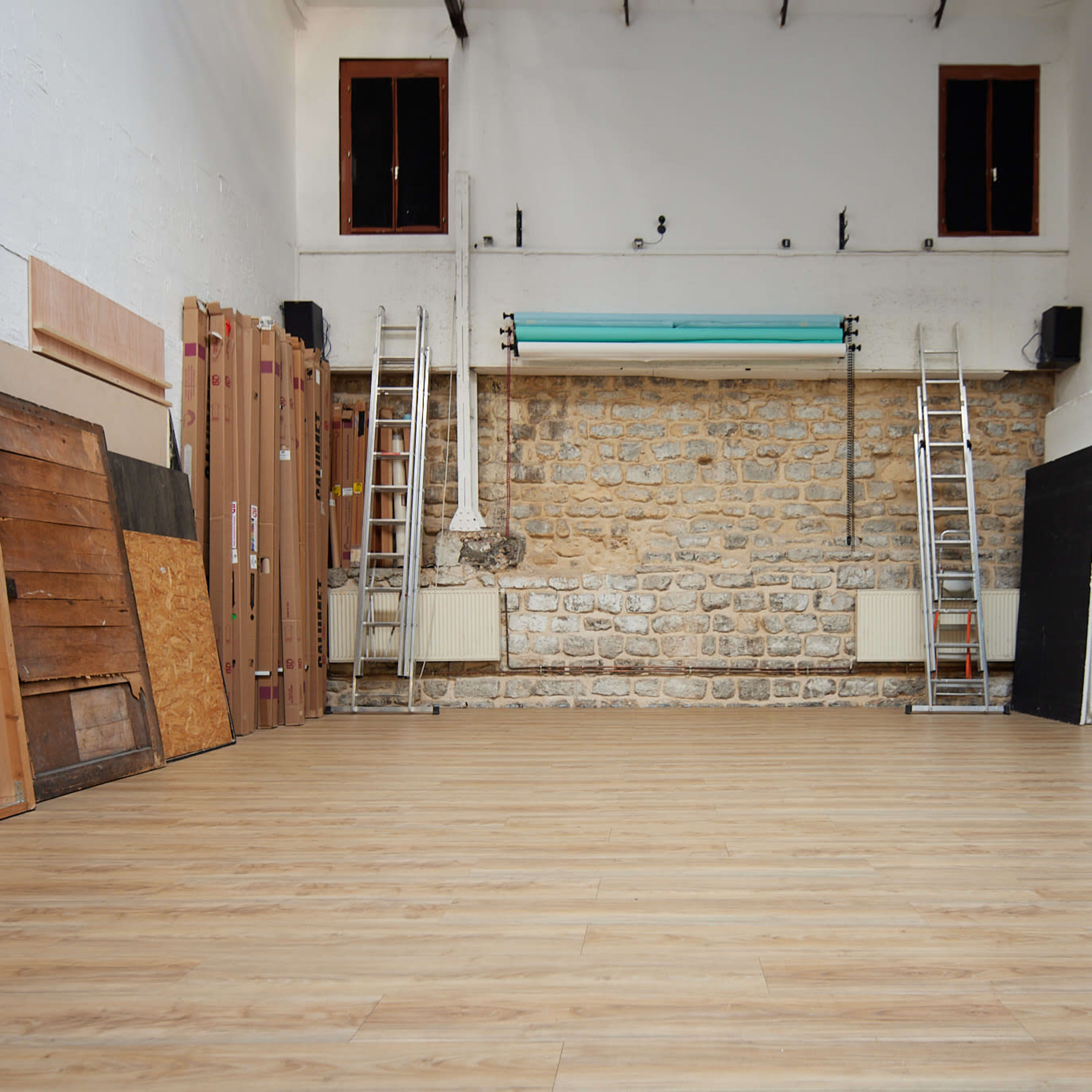 A spacious, empty room with wooden flooring, a stone wall at the back, and two ladders positioned on either side.