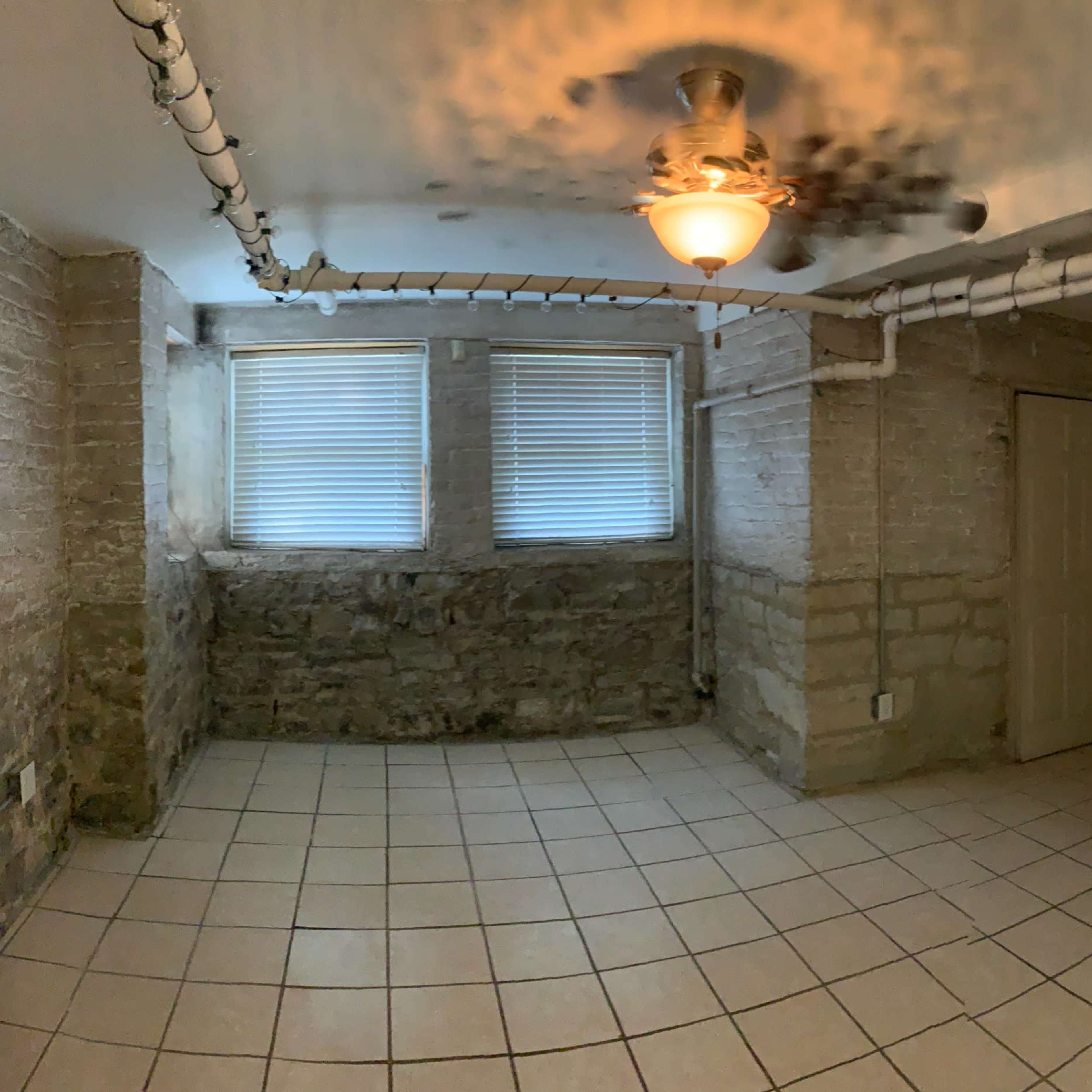 An empty room with exposed brick walls, tiled flooring, and three windows.