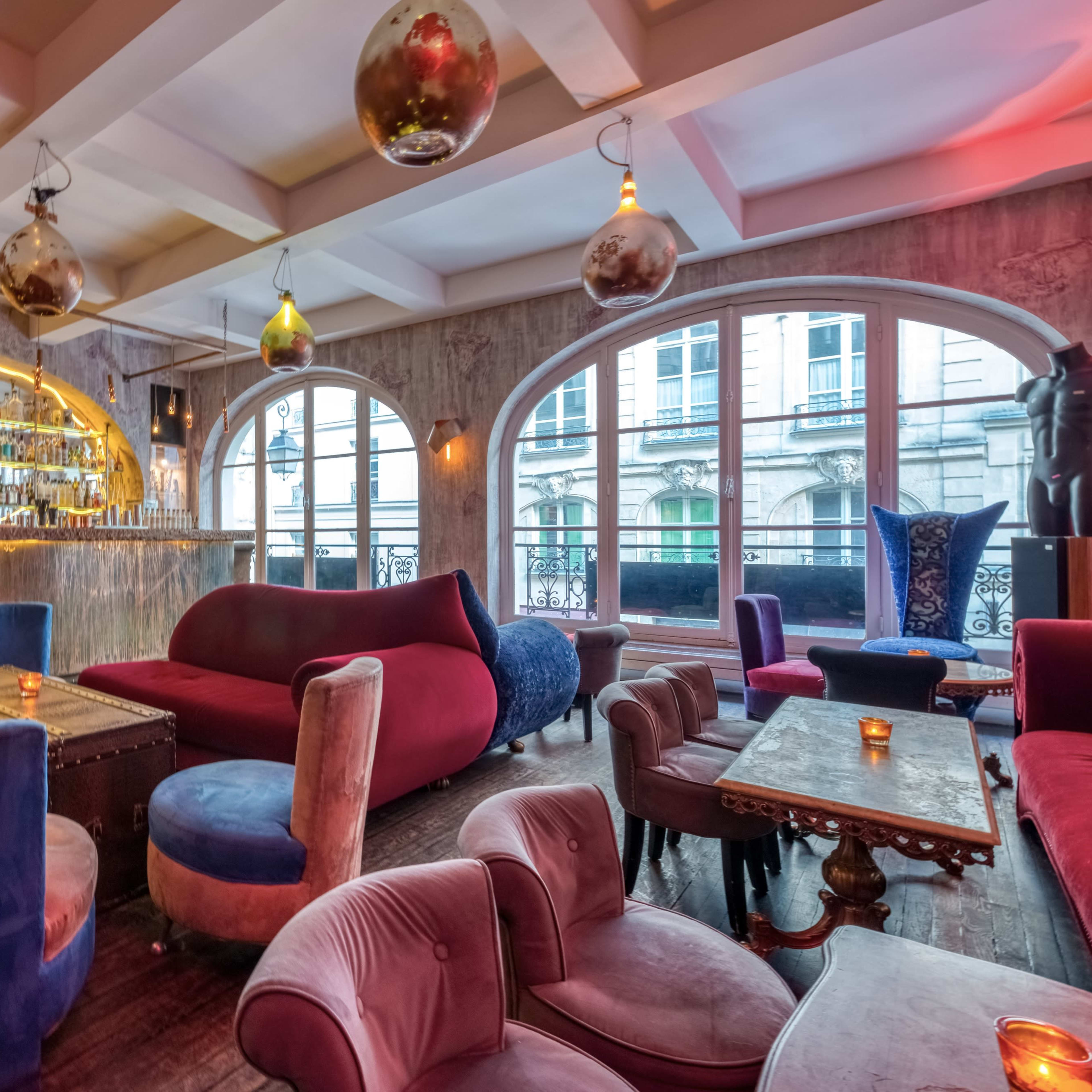 A stylish bar interior with plush seating, a circular bar backdrop, and large windows allowing natural light to enter the space.