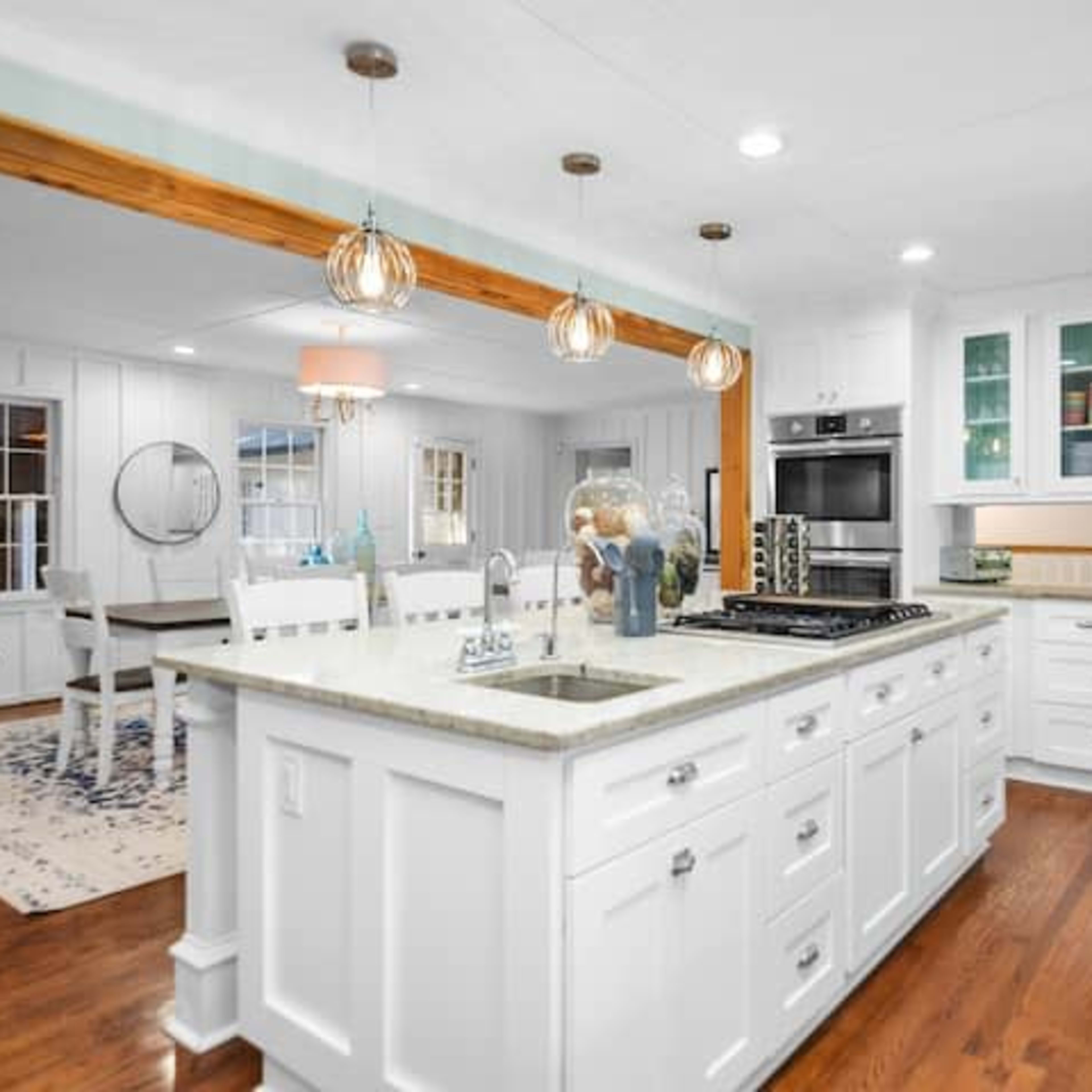 A modern kitchen with white cabinets, a central island with a gray countertop, and stainless steel appliances, opening into a dining area with a round table and chairs.