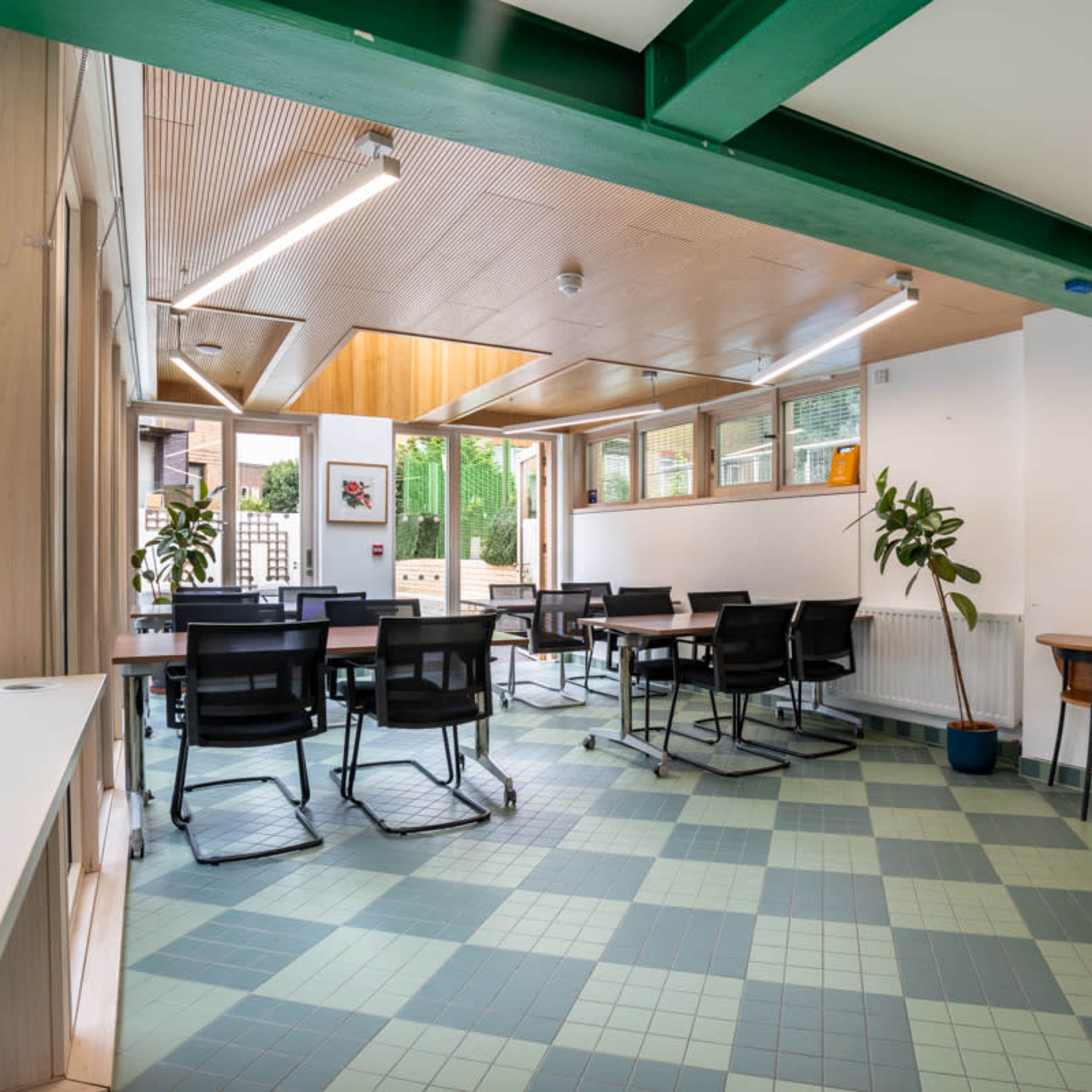 A well-lit room with tables and chairs arranged for meetings, featuring large windows that provide a view of greenery outside.