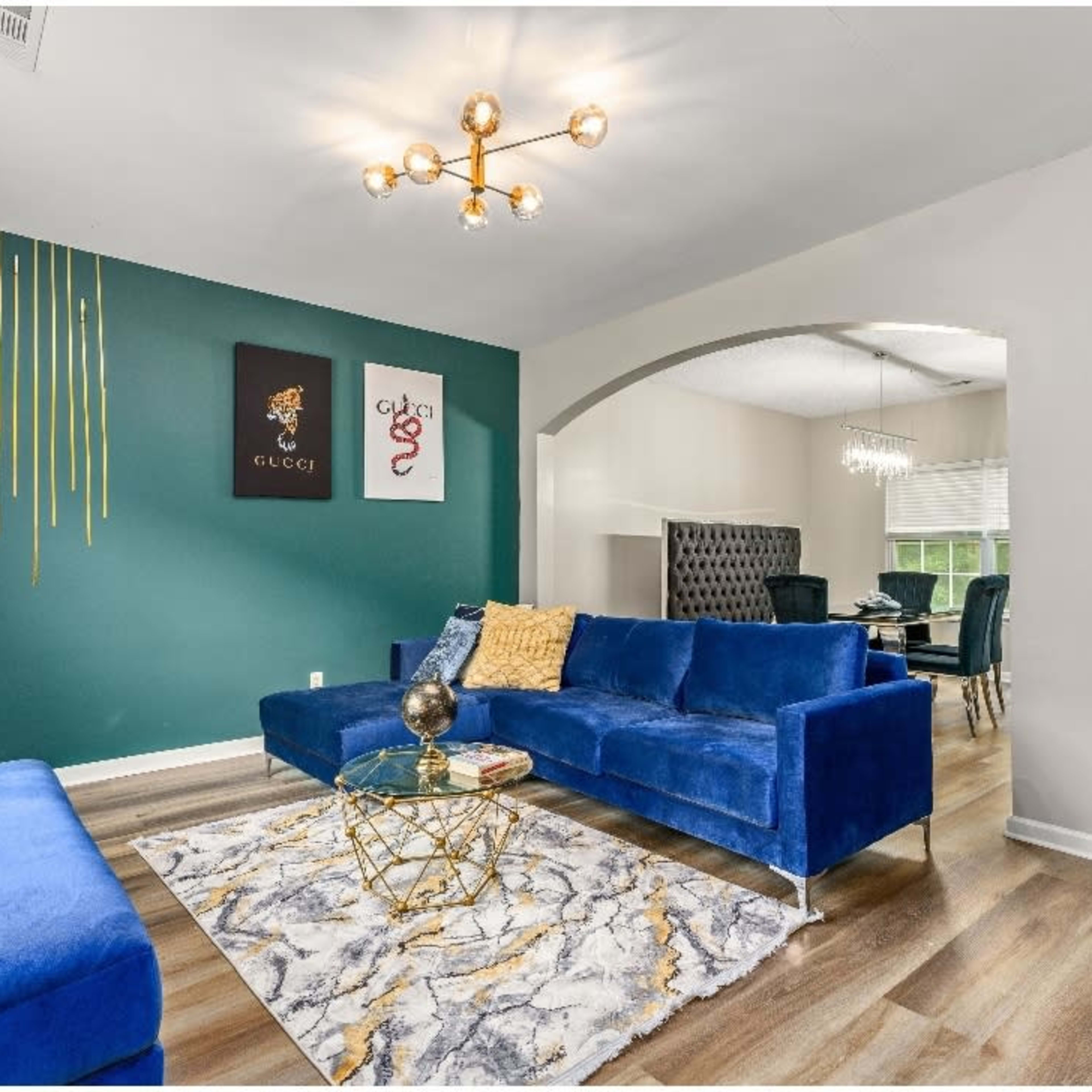 A modern living room featuring a blue velvet sofa, a geometric coffee table, and a decorative rug, with green and yellow accent walls.