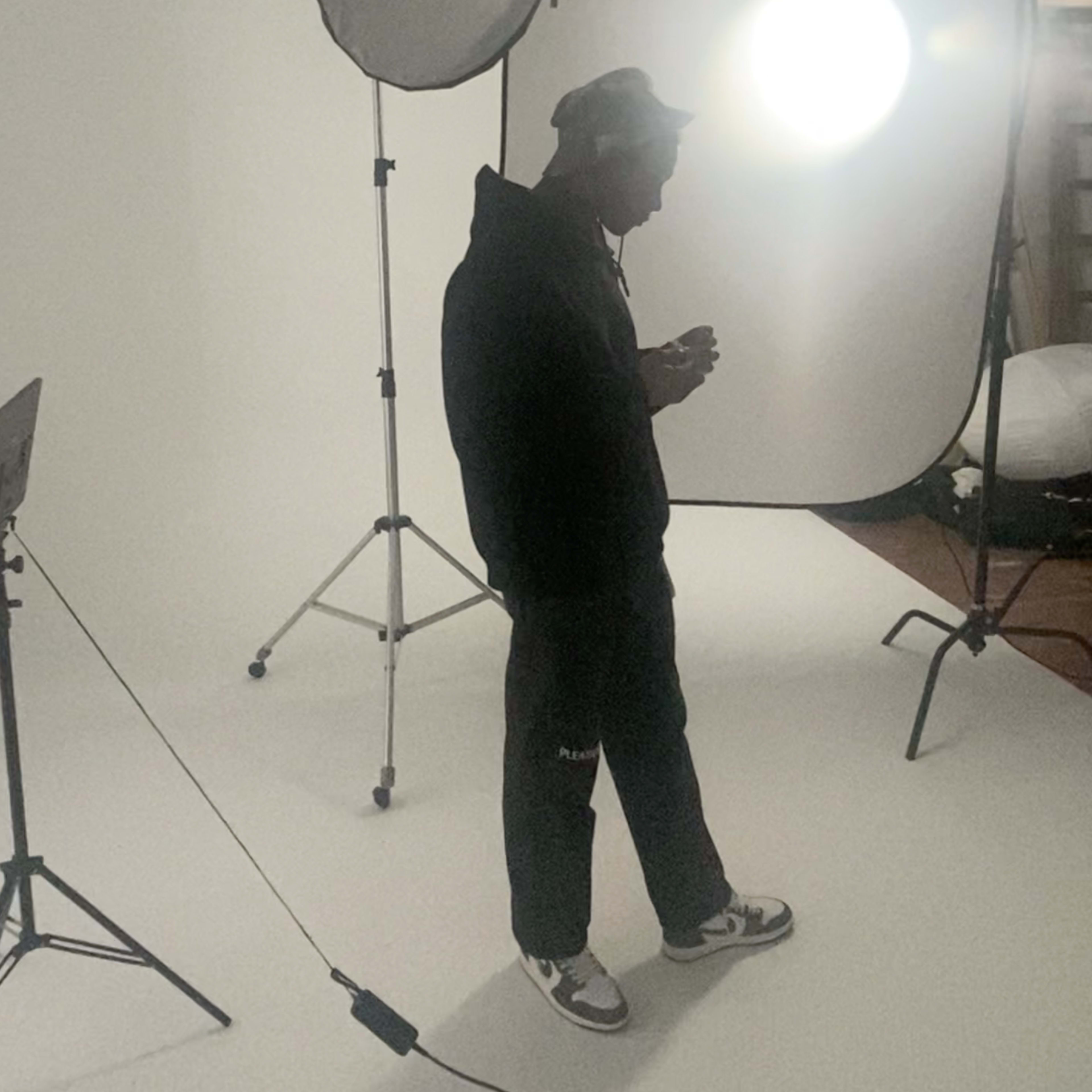 A person stands in a photography studio, framed by a white backdrop and lighting equipment.
