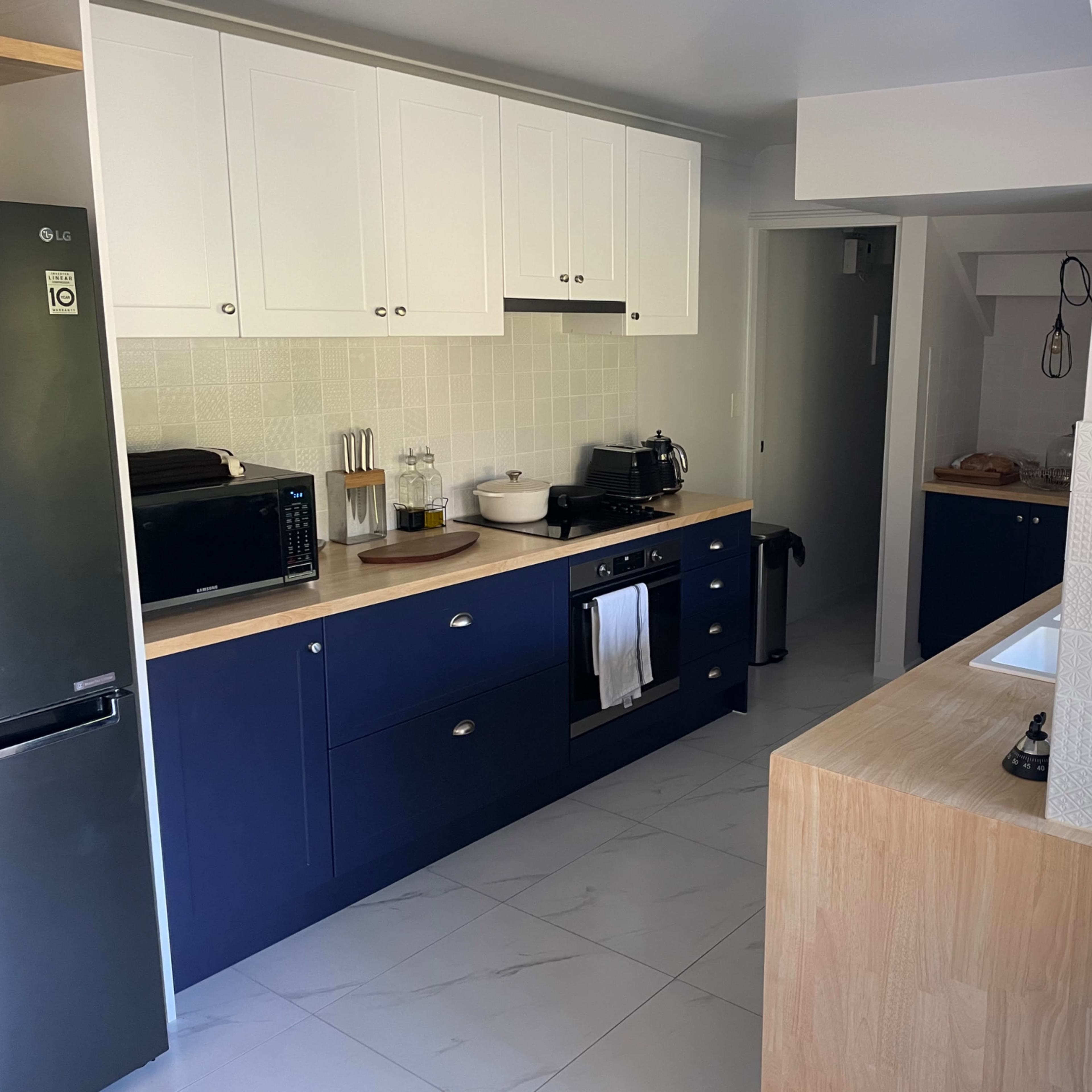 A modern kitchen with navy blue cabinetry, wooden countertops, and white tile accents.