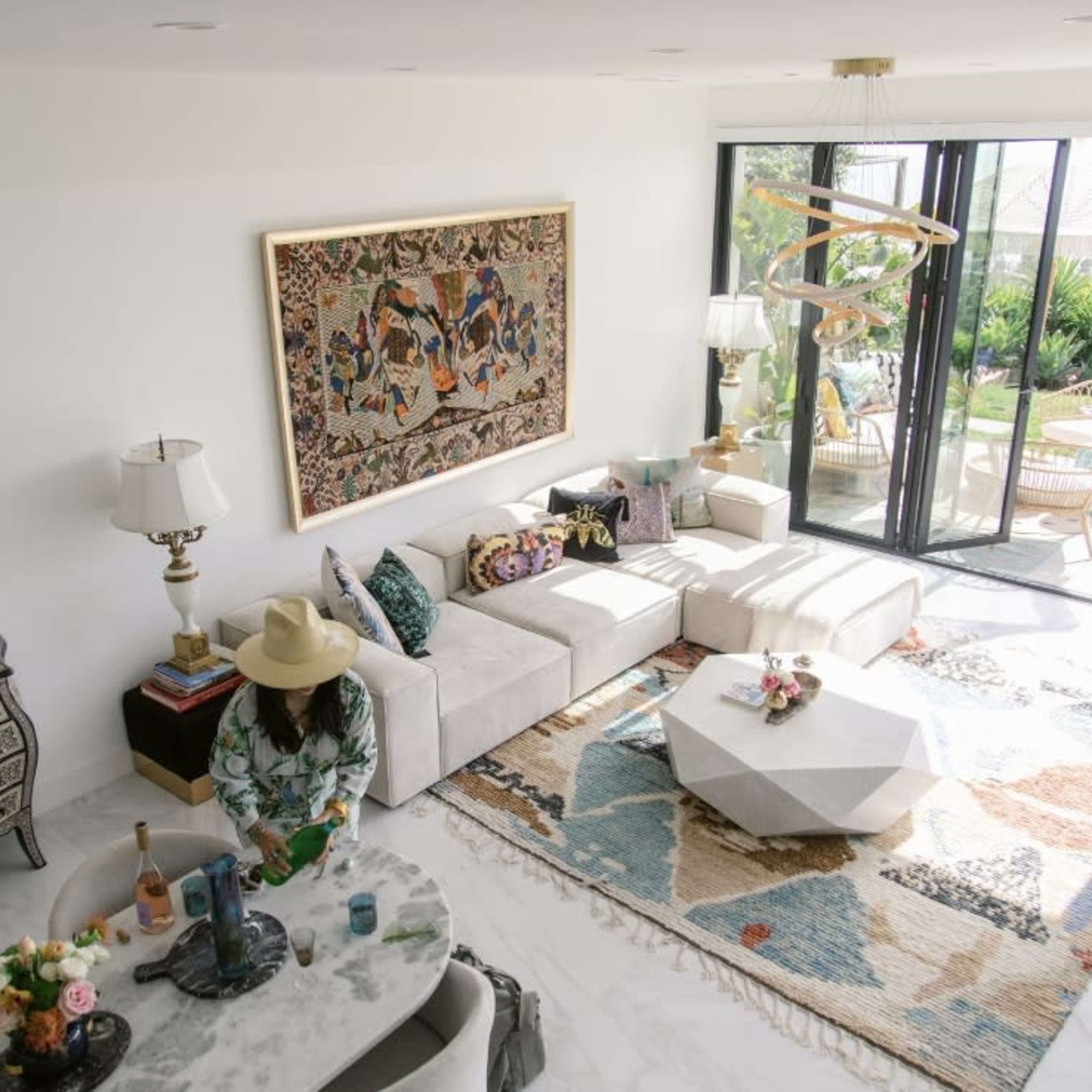 A bright living room features a white sectional sofa, a patterned rug, a coffee table, and large glass doors leading to an outdoor patio.