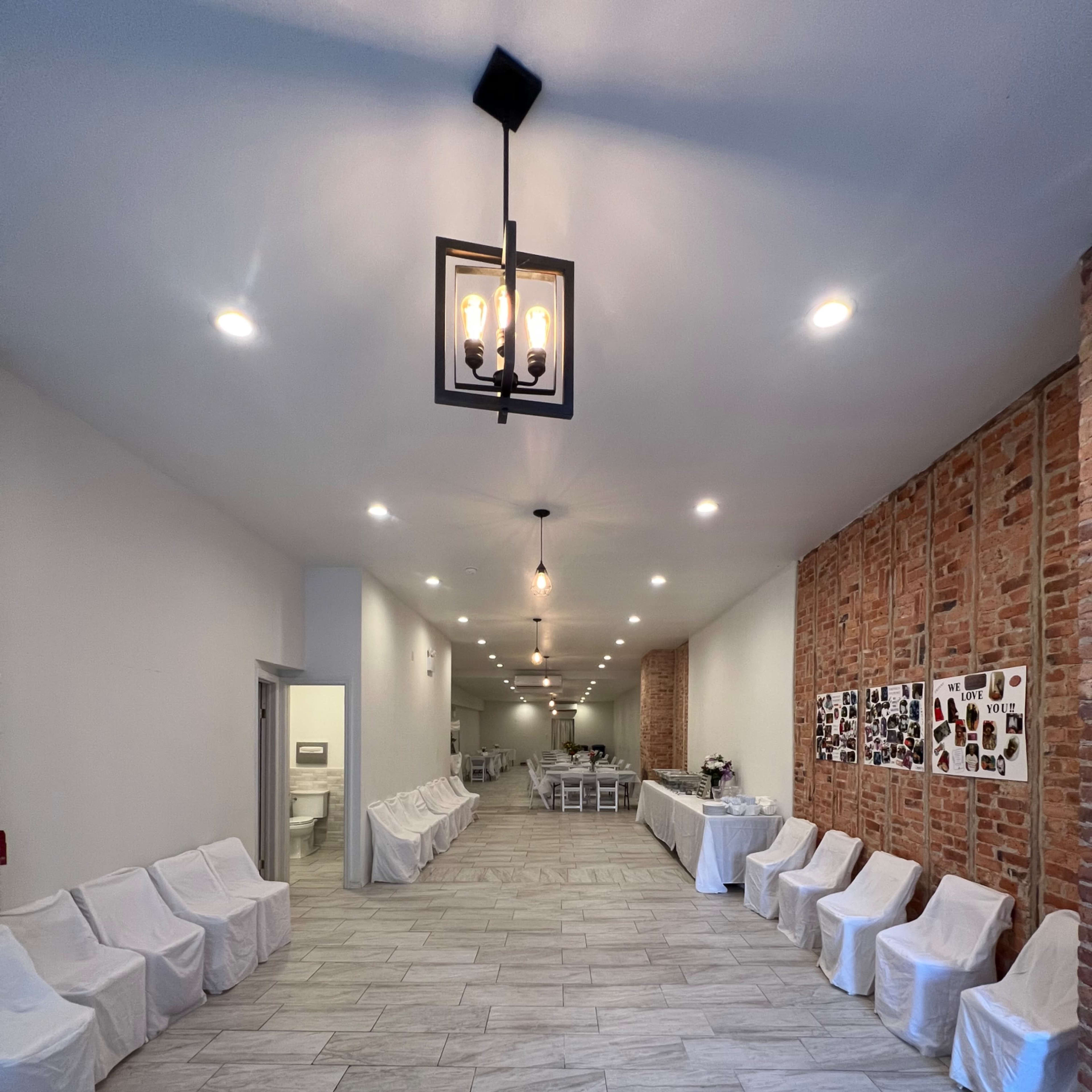 A long, narrow hall with covered chairs lined along each side and a brick wall featuring framed pictures.
