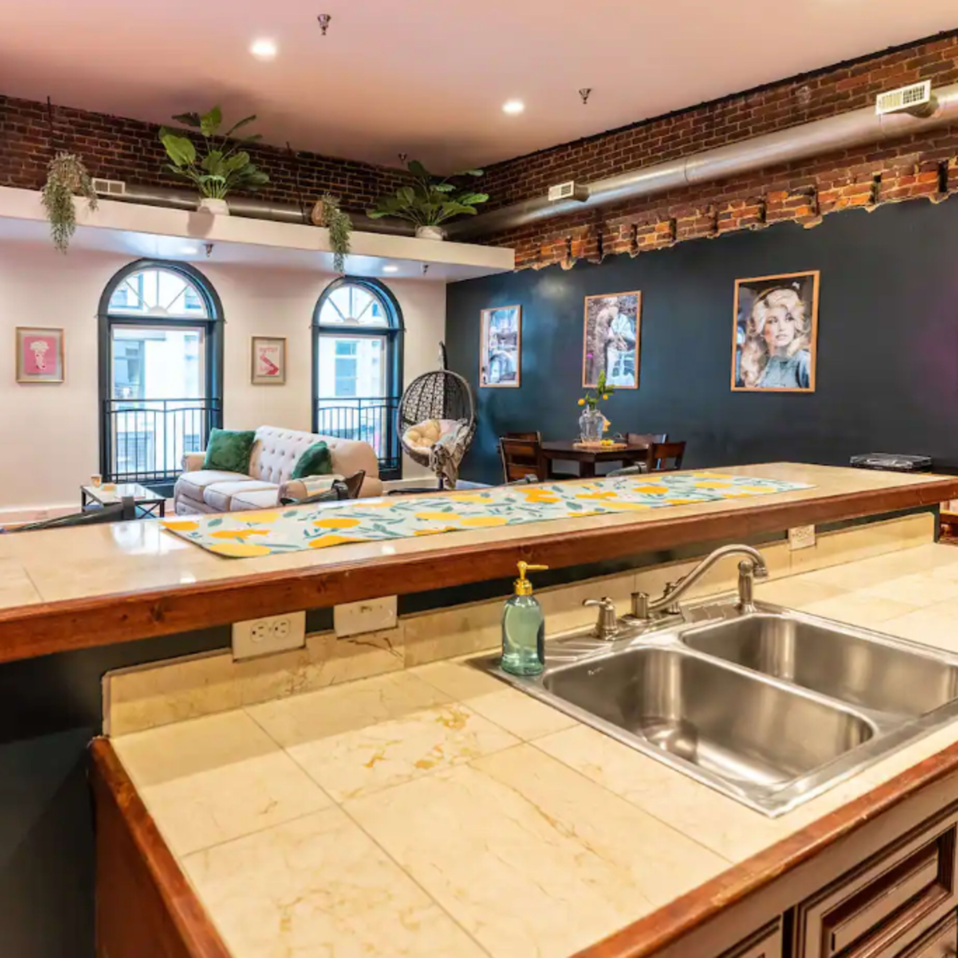 An open-concept living space featuring a kitchen island with a sink, a seating area with a couch and chairs, and large windows with arching designs.