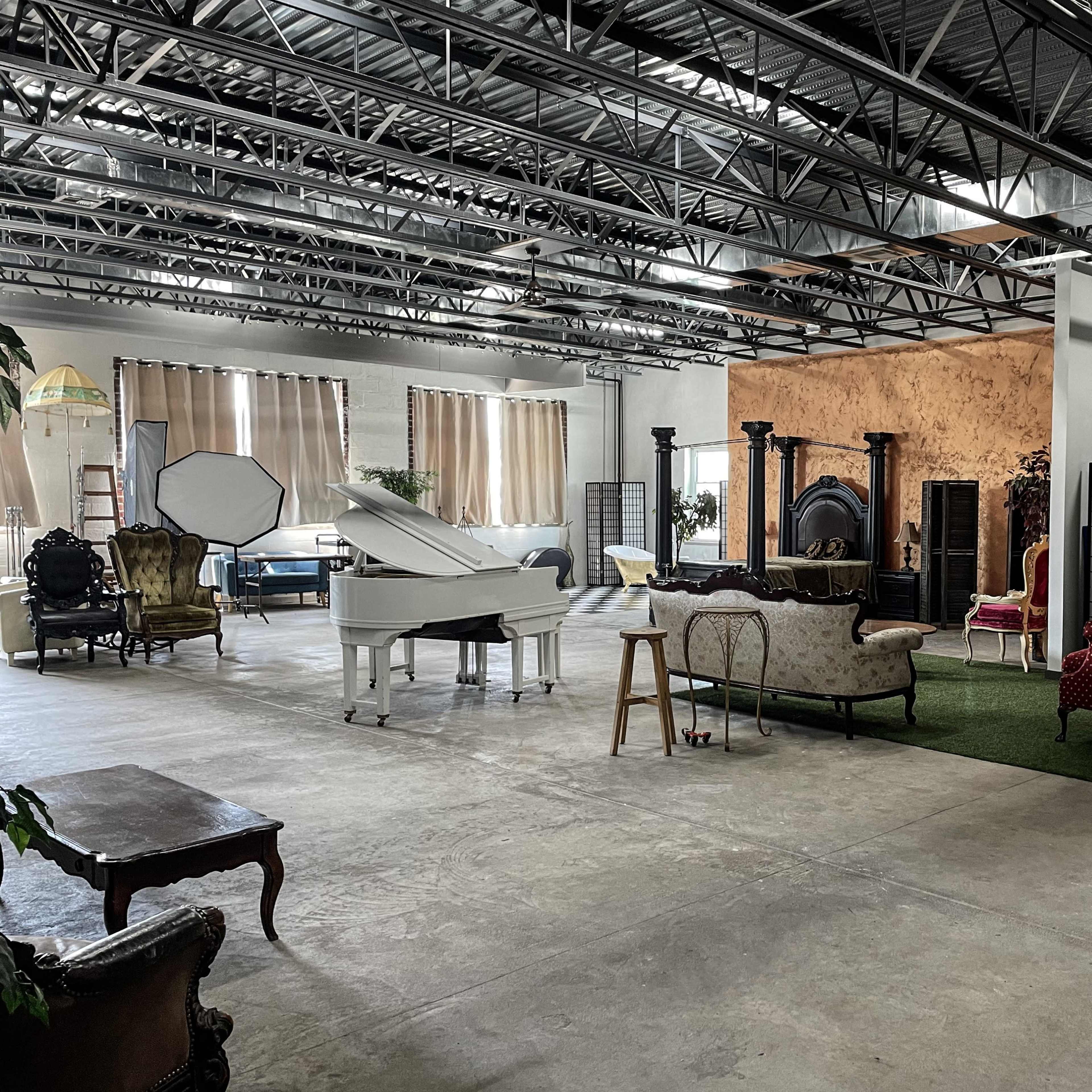 A spacious studio with a grand piano, various seating areas, and decorative elements like plants and a brick wall.