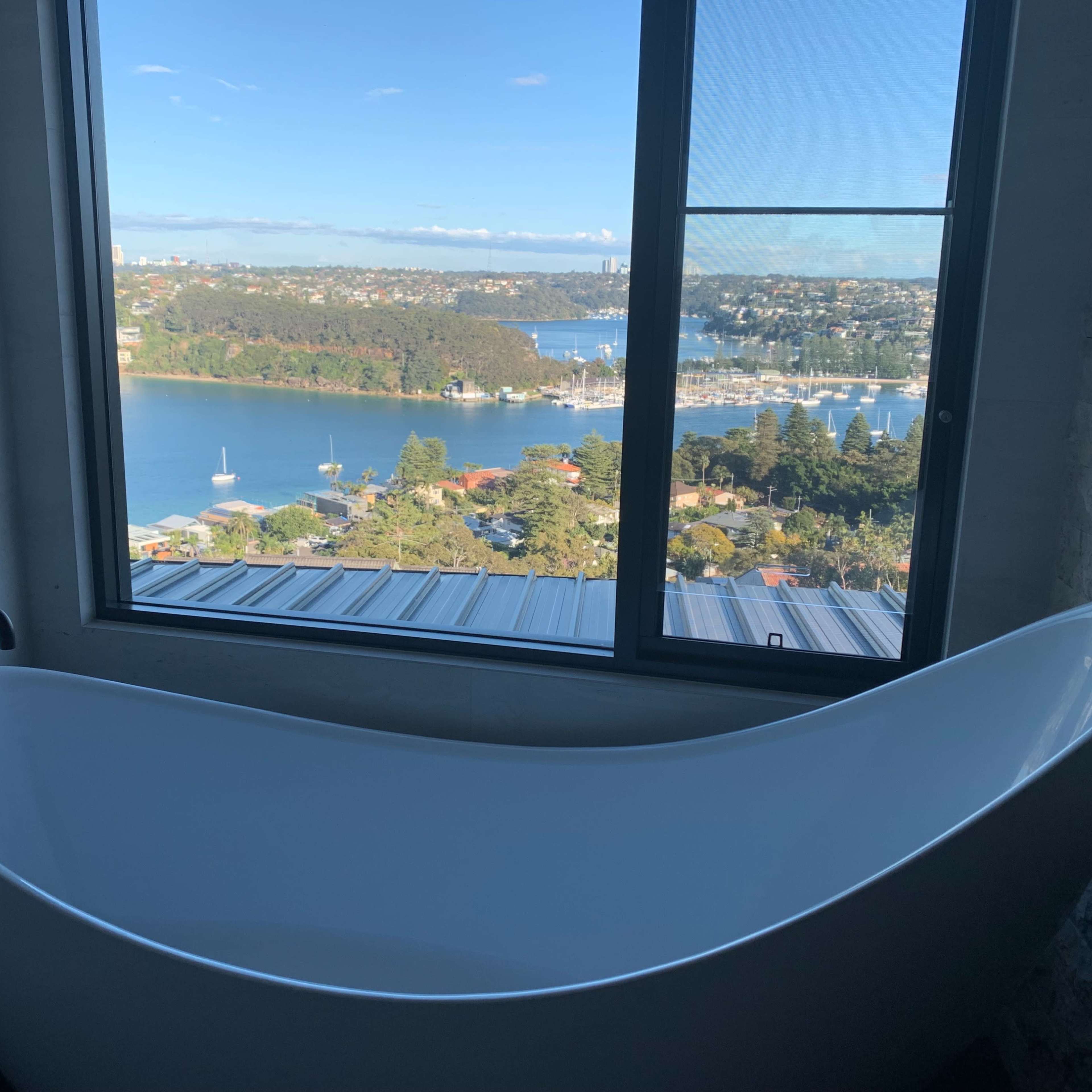 A white freestanding bathtub is positioned next to a large window offering a view of a bay and surrounding landscape.