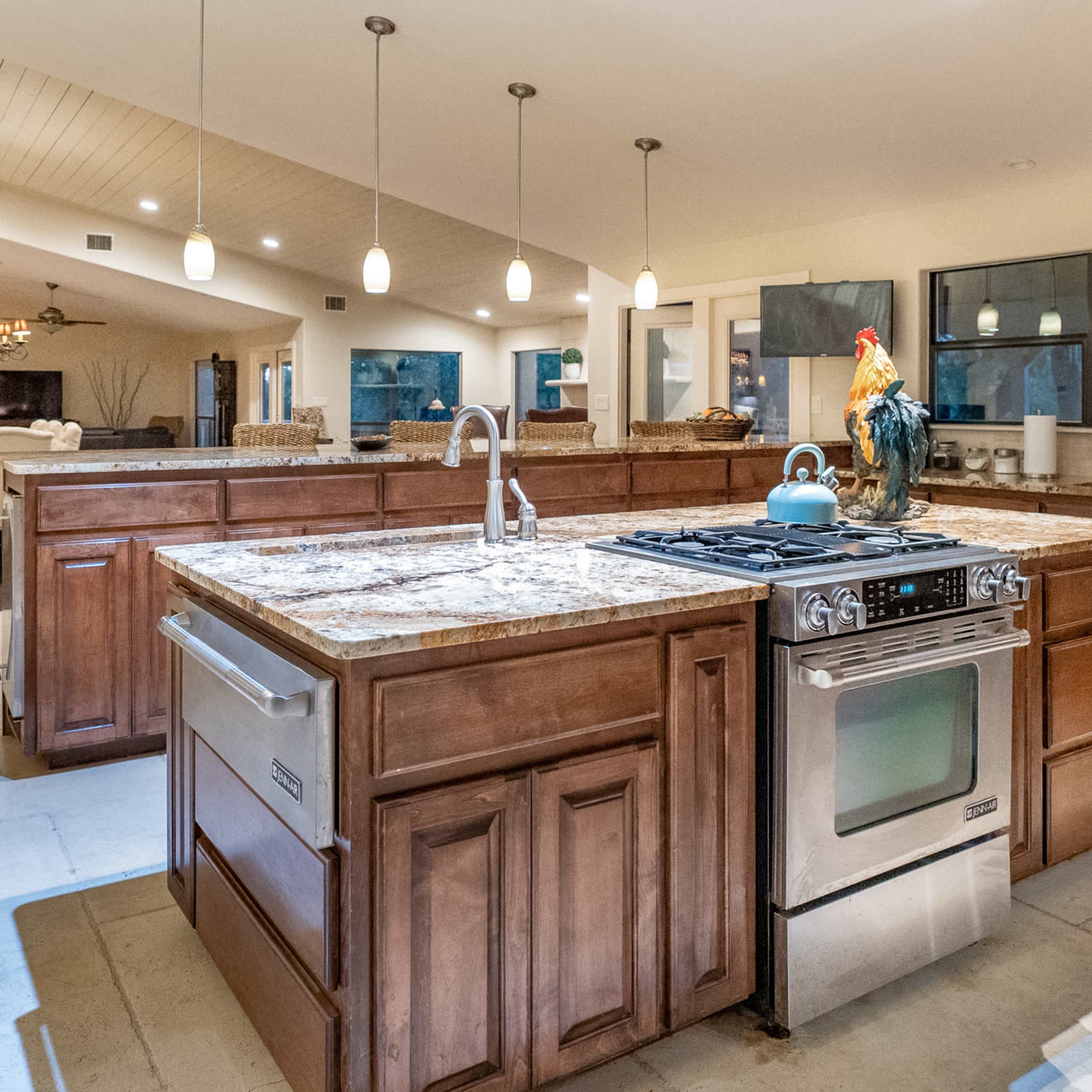 The spacious kitchen features a large wooden island with a gas stove, stainless steel appliances, and pendant lighting above.