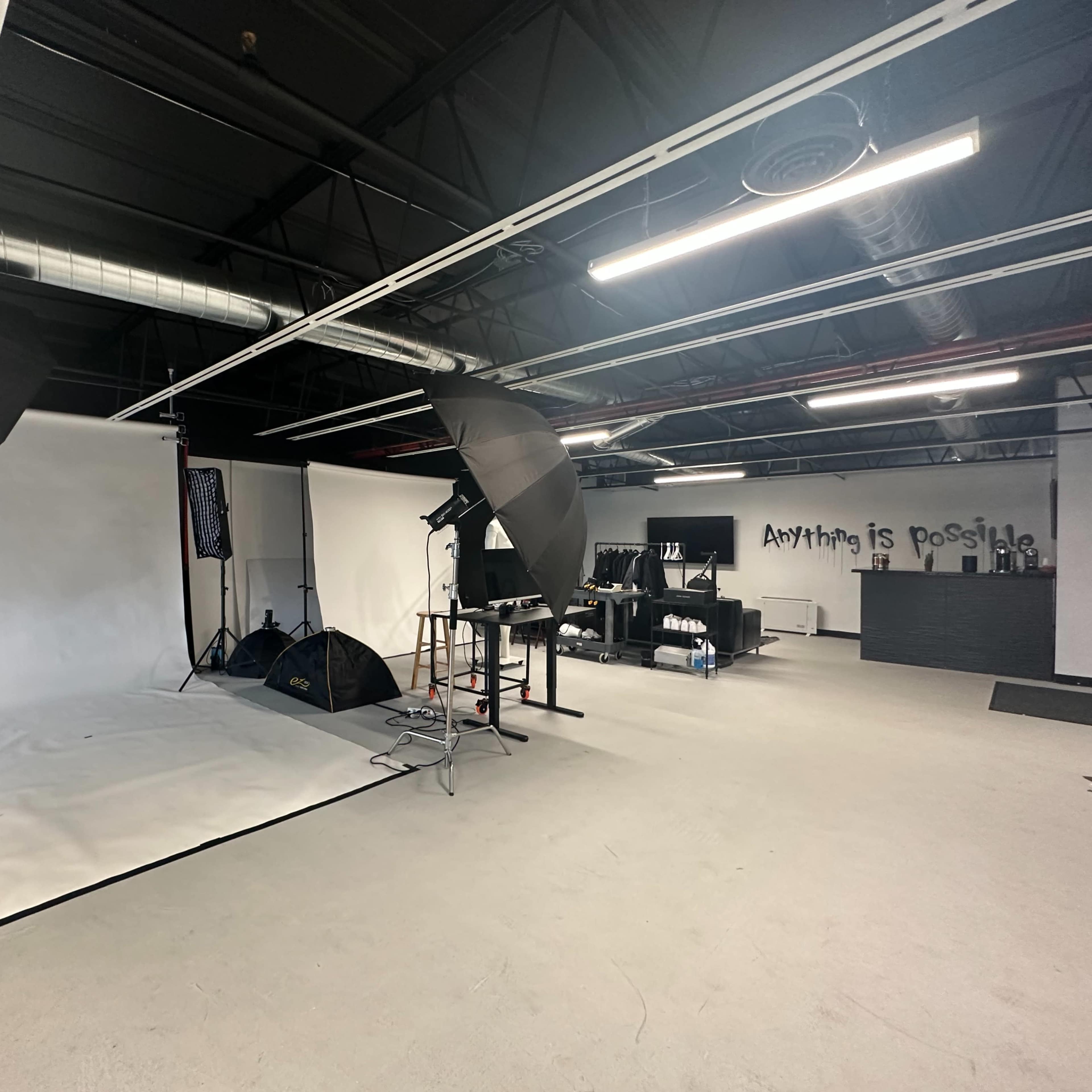 A photography studio equipped with lighting equipment, a blank backdrop, and a minimalistic workspace with a wall displaying the phrase "Anything is possible."