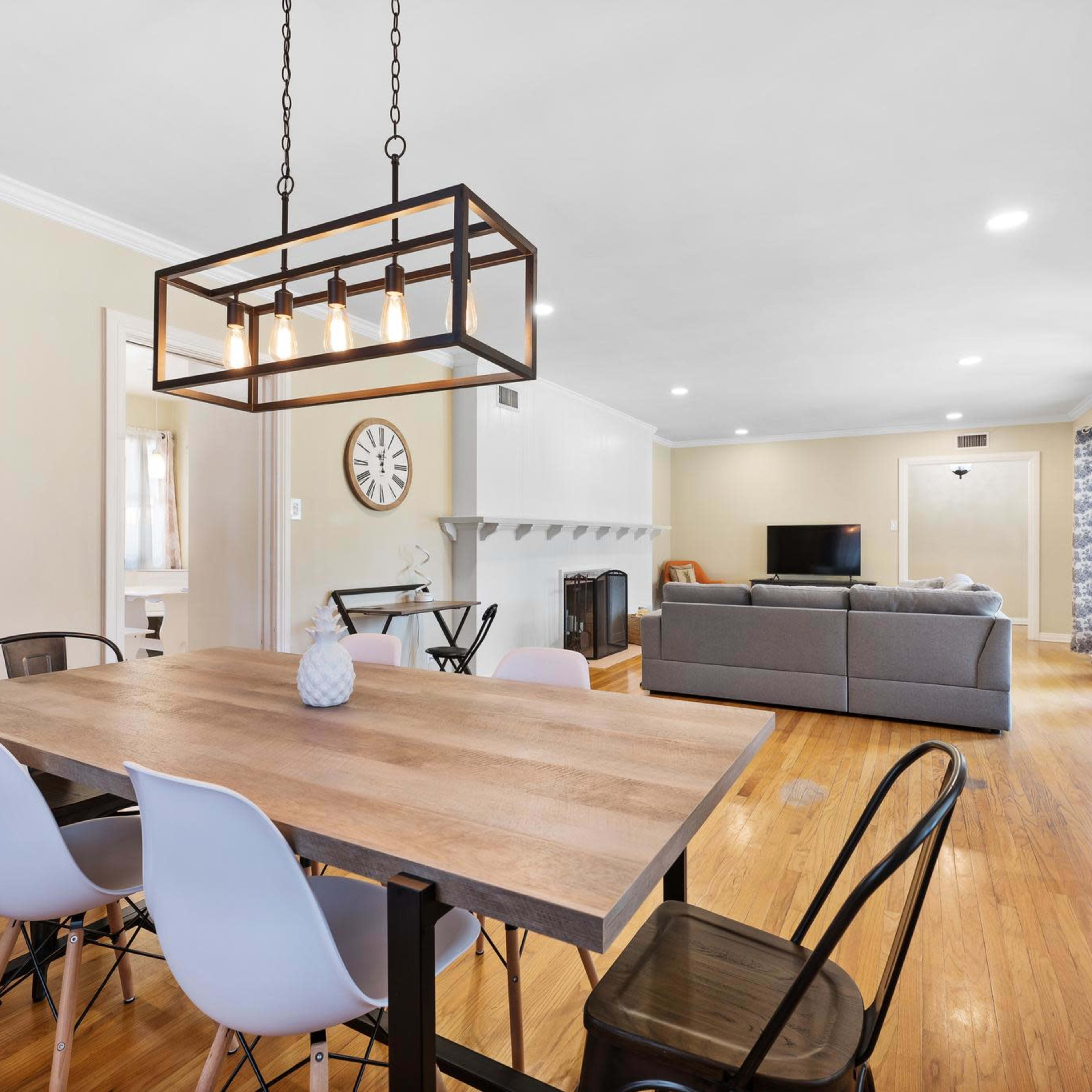 A spacious dining area features a wooden table with modern chairs, leading into a well-lit living room with a gray sofa and television.
