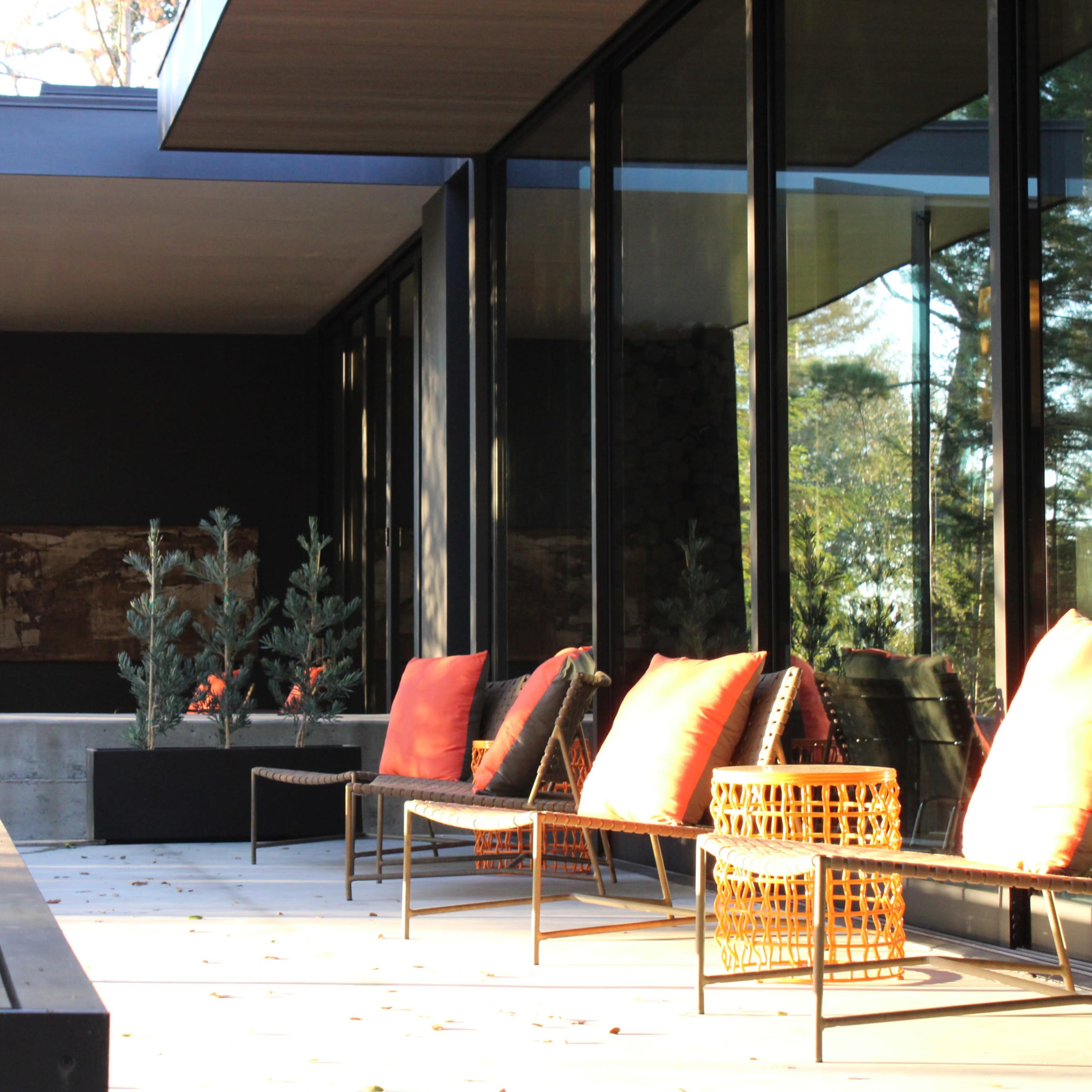 A modern terrace with a wooden railing, several outdoor chairs with orange cushions, and potted plants in a landscaped setting.