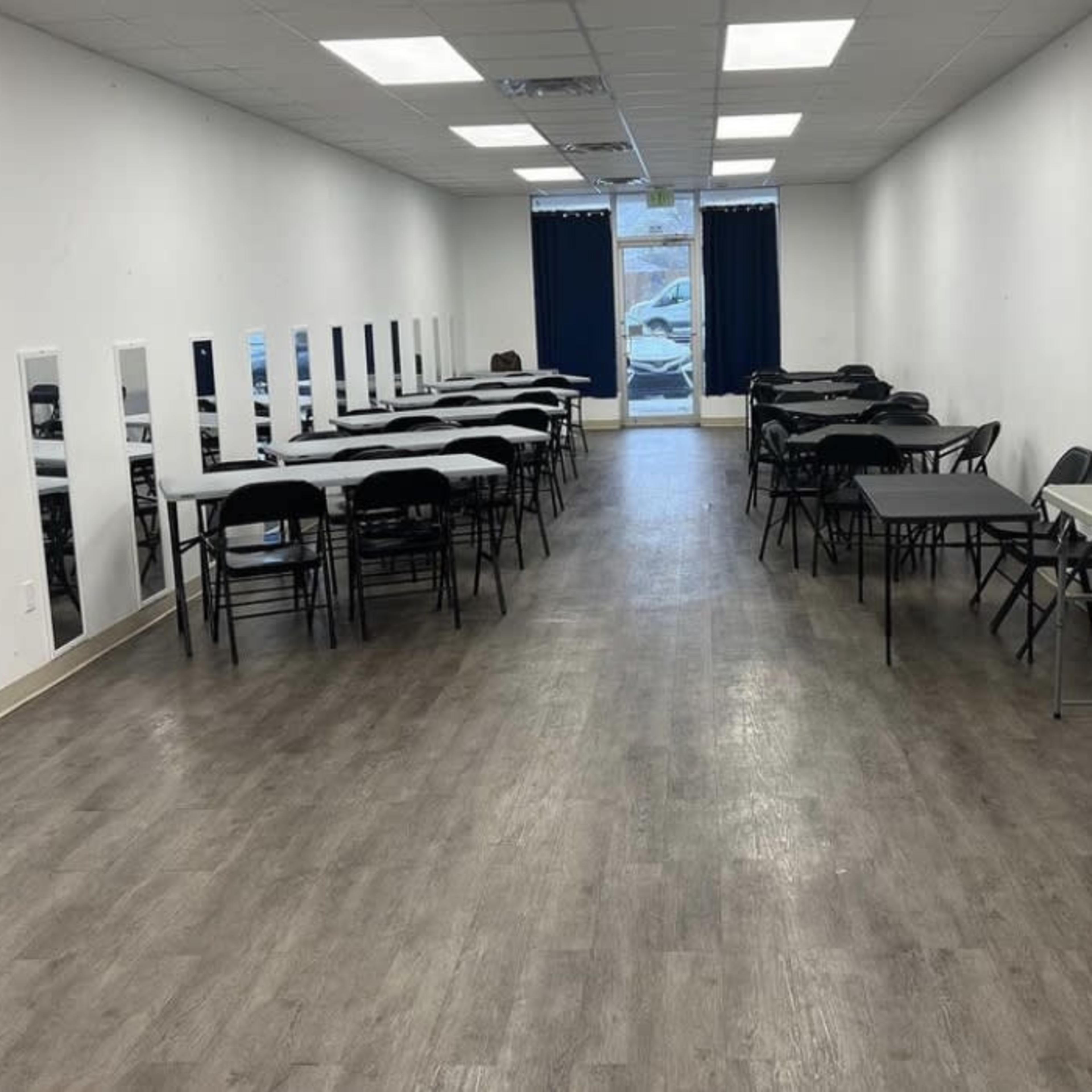 A long, narrow room set up with several tables and chairs, with mirrors along one side and a doorway at the far end.