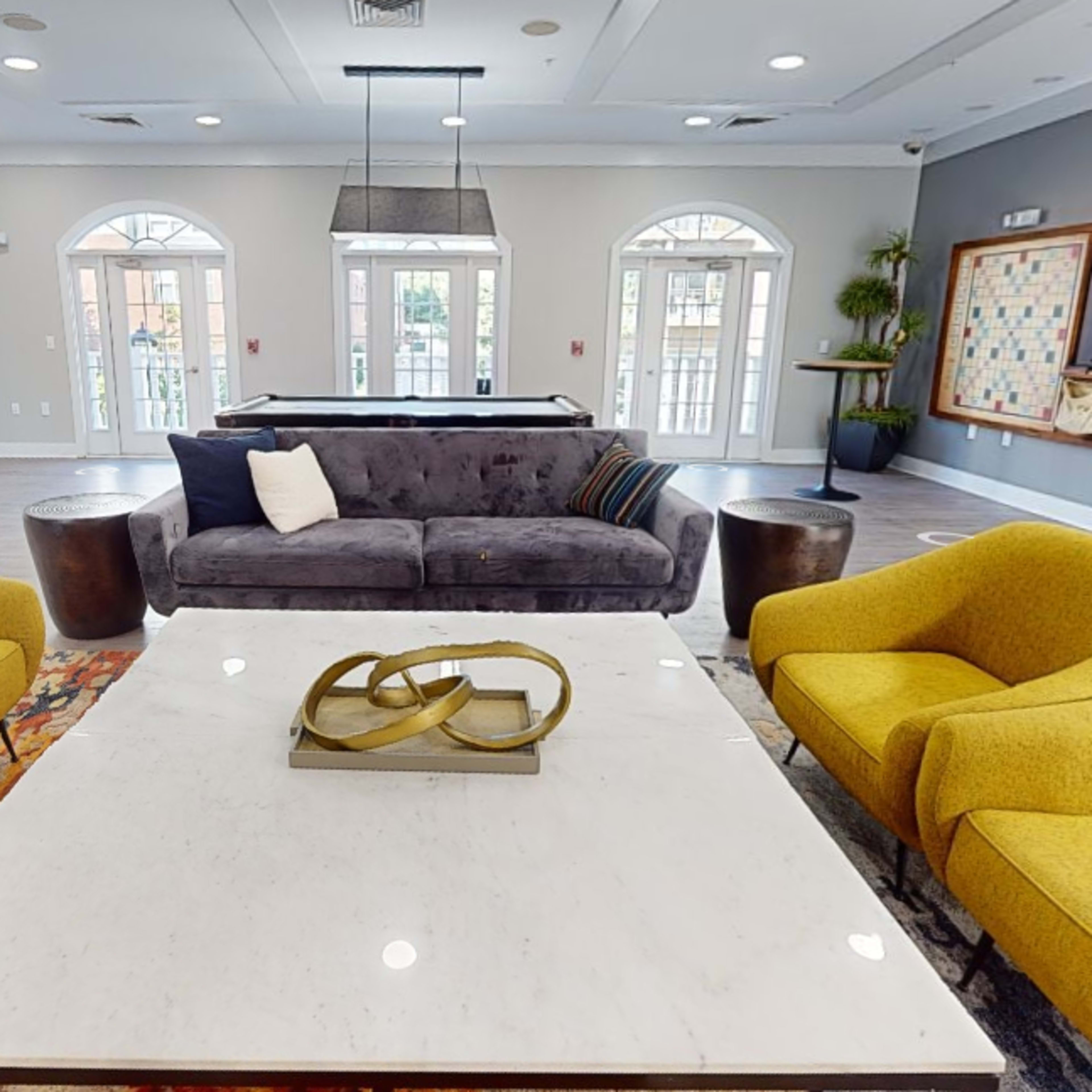 A modern lounge area with a gray sofa, two yellow armchairs, and a large marble coffee table, surrounded by large windows.