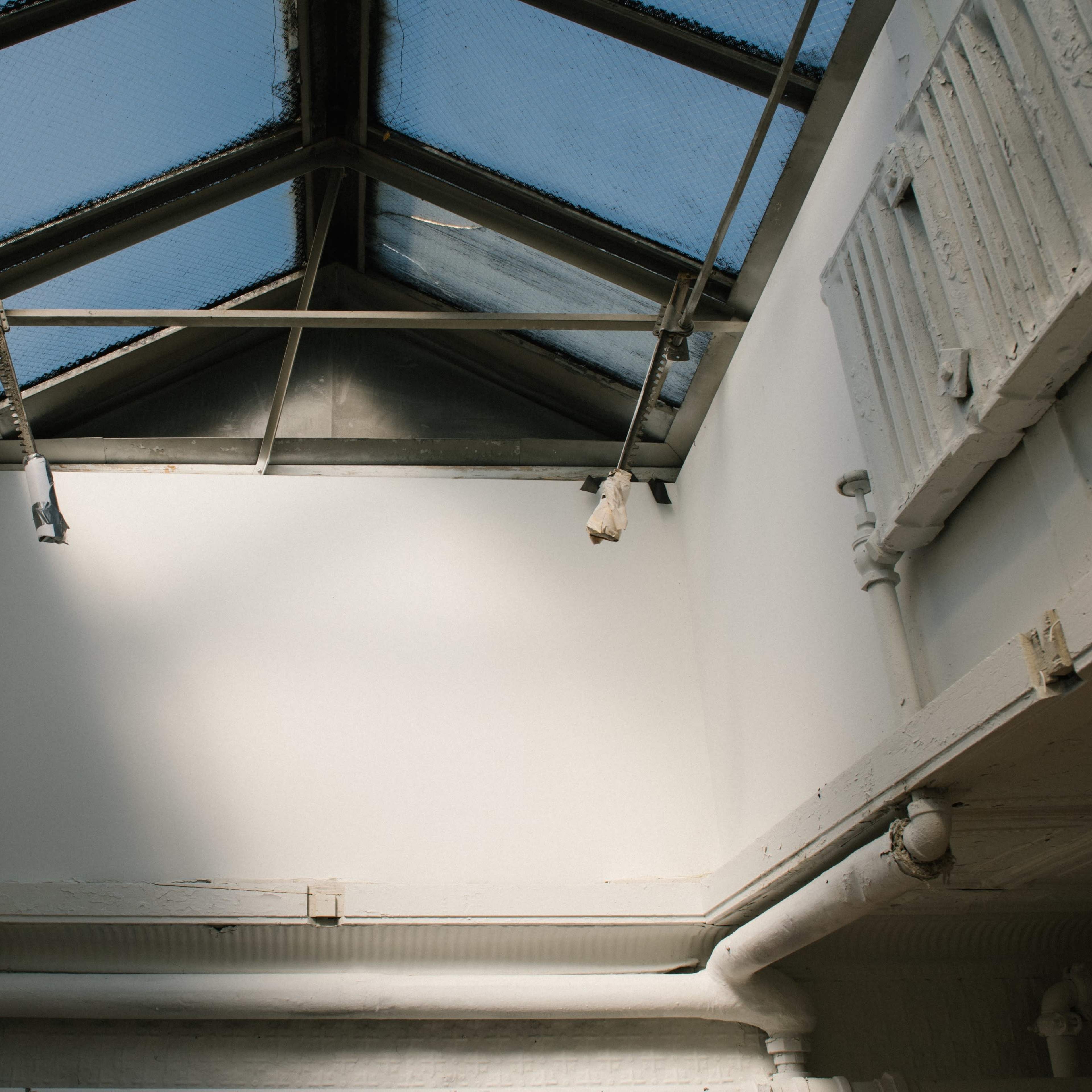 An interior space with a skylight, revealing a ceiling and walls that are lightly colored, along with exposed pipes and radiators.