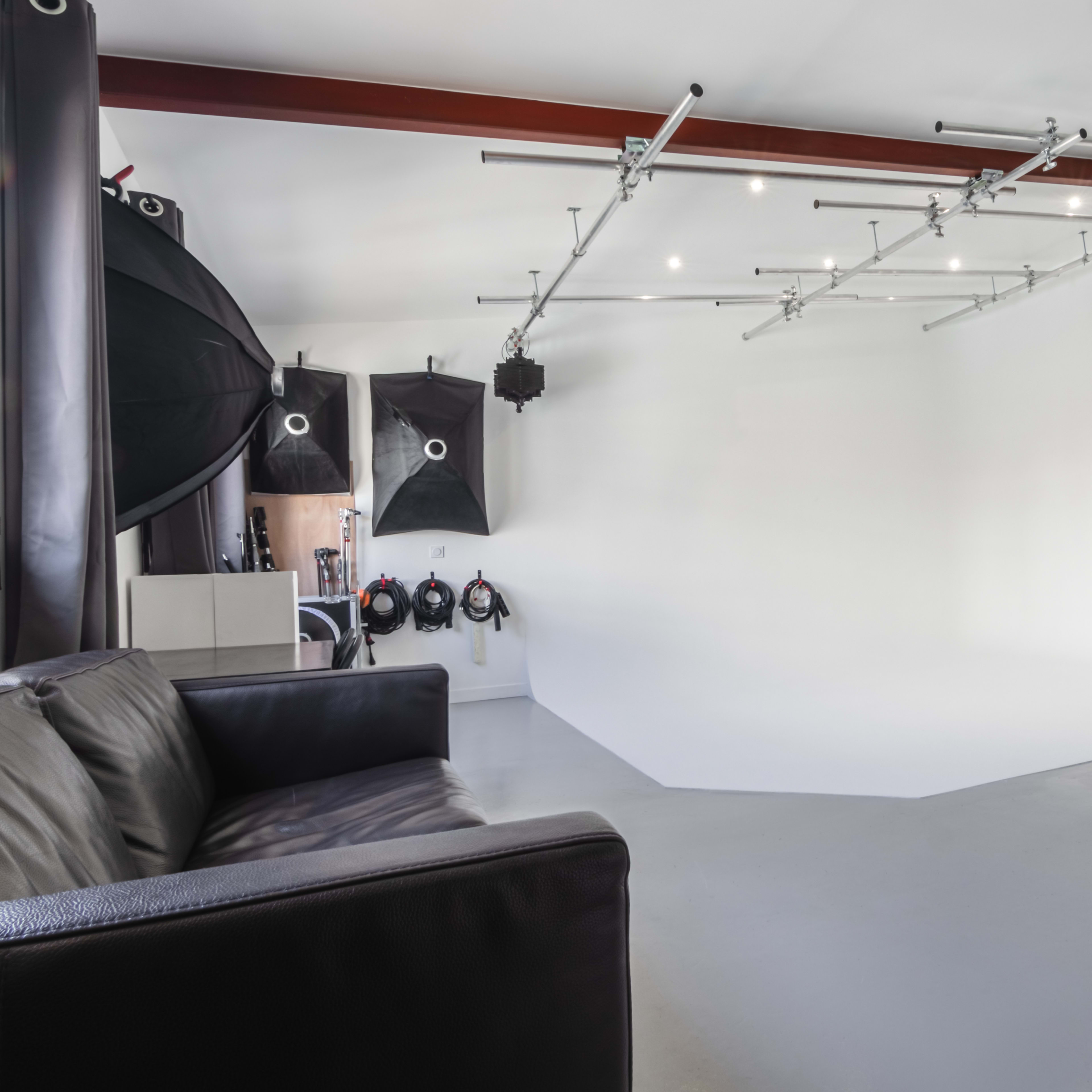 A photography studio with a seamless white backdrop, professional lighting equipment, and a black sofa in the foreground.