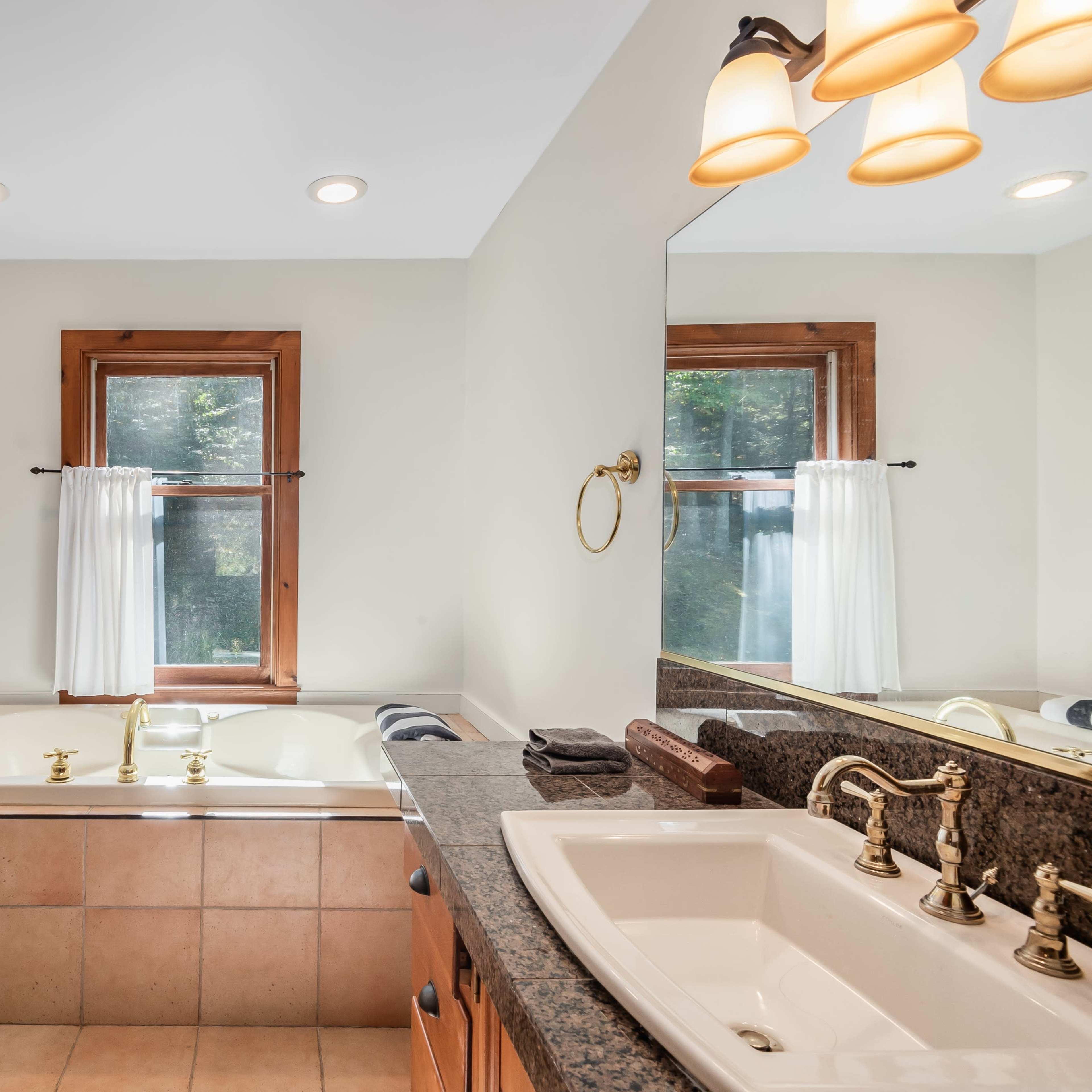 A bathroom featuring a bathtub next to a large window, a sink with a dark countertop, and a wooden door.