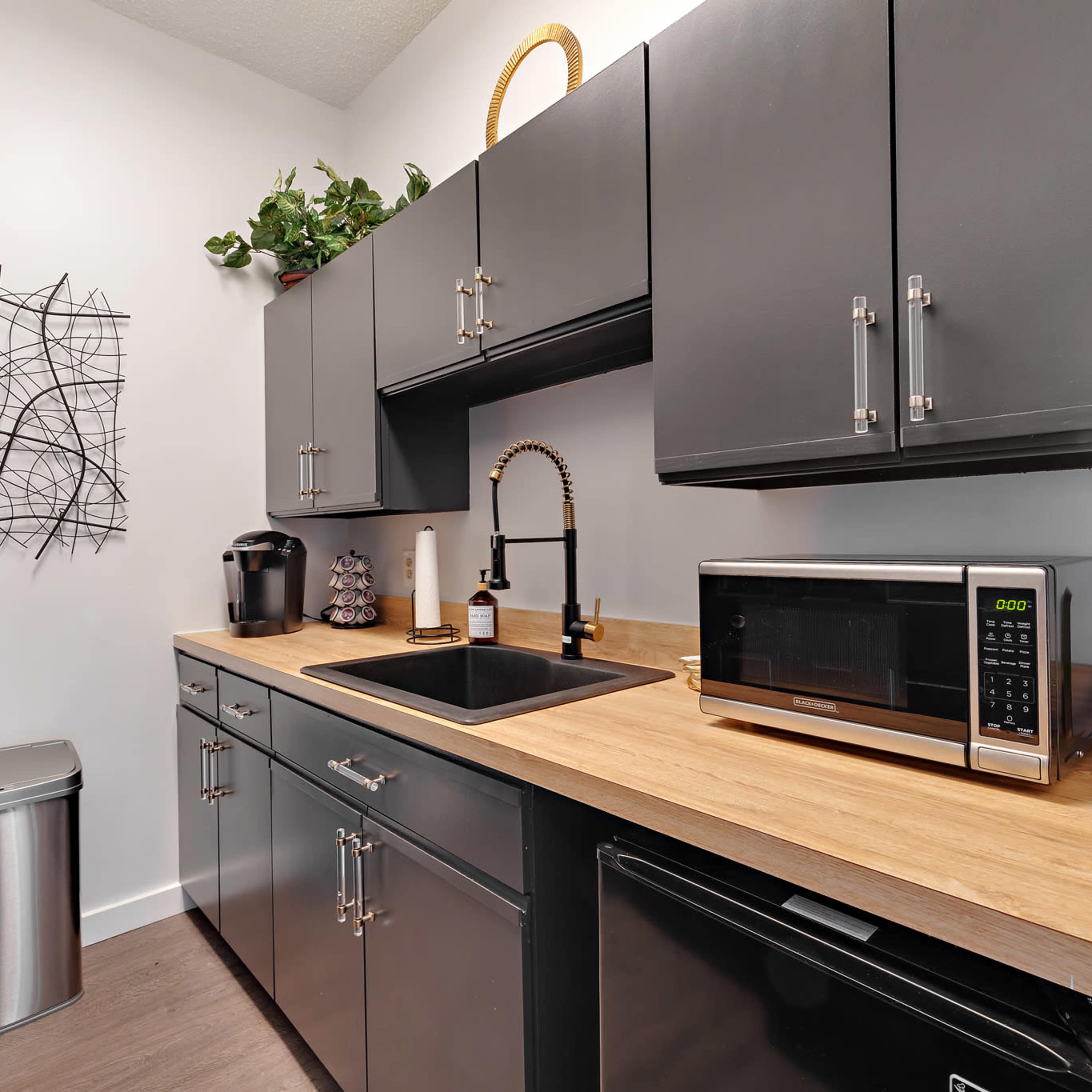 A modern kitchen featuring dark cabinets, a wooden countertop, a sink, a microwave, and an organized arrangement of appliances and decorative elements.